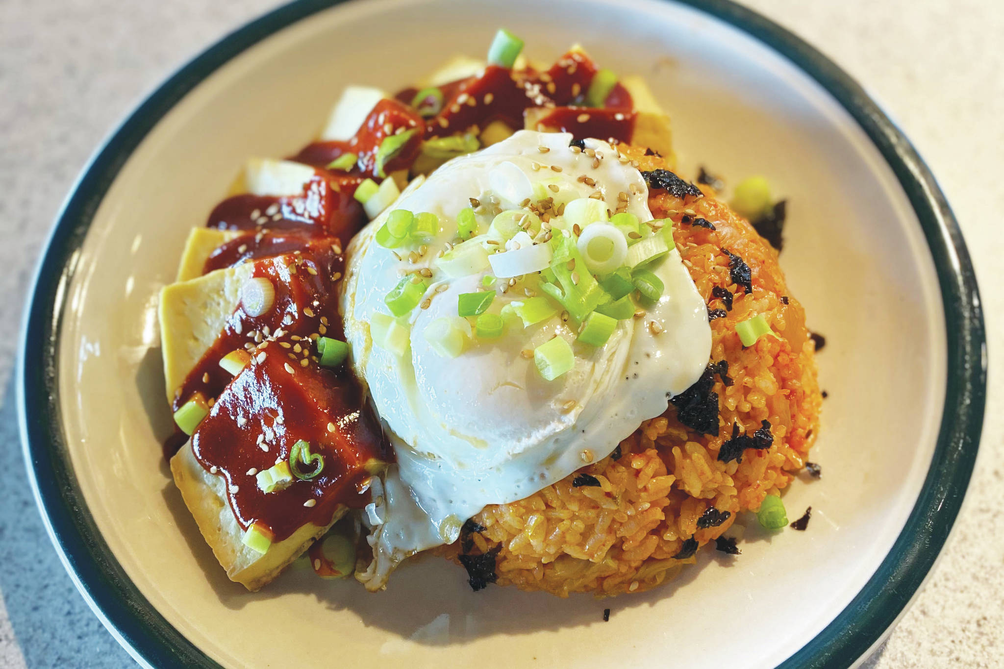 A fried egg, crushed seaweed paper, green onions and sesame seeds top this classic Korean kimchi dish. (Photo by Tress Dale/Peninsula Clarion)