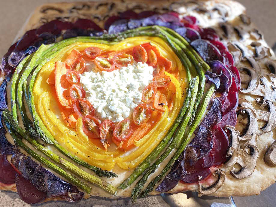 Feta and Parmesan cheese, cherry tomatoes, carrot, yellow bell pepper, asparagus, purple potatoes, beets and white button mushrooms are shaped into a rainbow with a cheesy heart on top of focaccia bread. (Photo by Tressa Dale/Peninsula Clarion)