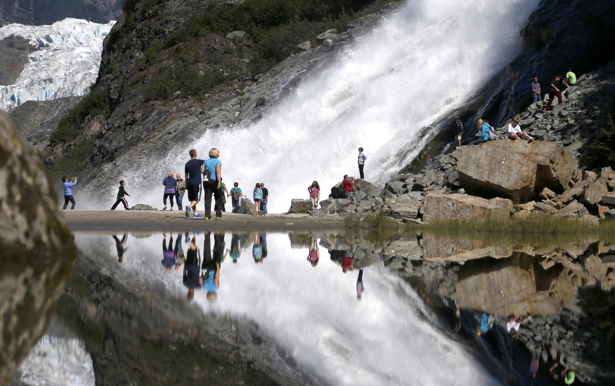 In this July 31, 2013, file photo, tourists visiting the Mendenhall Glacier in the Tongass National Forest are reflected in a pool of water as they make their way to Nugget Falls in Juneau. The federal government has announced plans to repeal or replace a decision by the Trump administration to lift restrictions on logging and road building in a southeast Alaska rainforest that provides habitat for wolves, bears and salmon. The U.S. Department of Agriculture’s plans for the Tongass National Forest were described as consistent with a January 2021 executive order from President Joe Biden that called for reviewing agency actions during the Trump administration that could be at odds with Biden’s environmental priorities. (AP Photo/Charles Rex Arbogast, File)