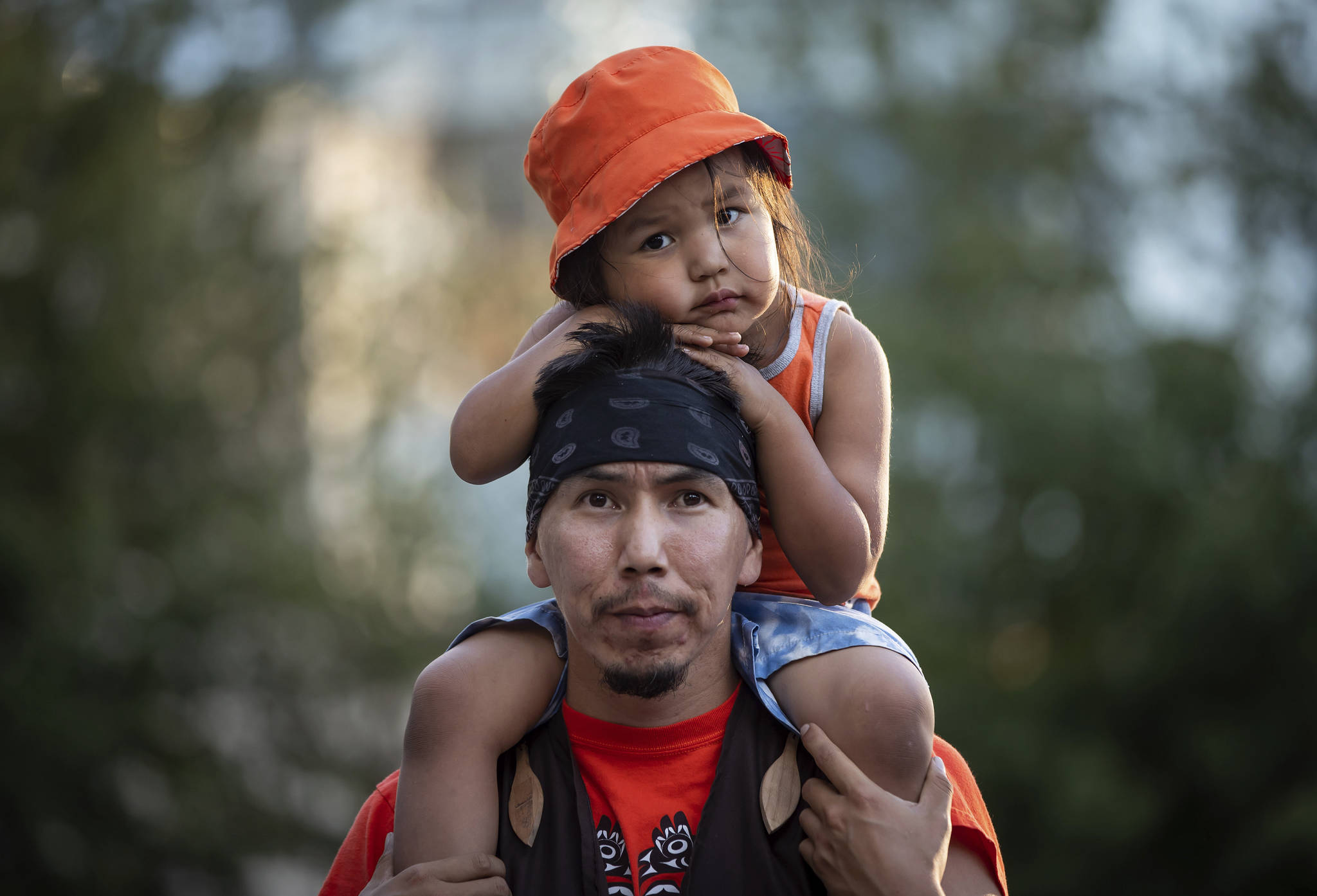 Cowichan Tribe member Benny George holds his child Bowie, 3, on his shoulders as they listen during a ceremony and vigil for the 215 children whose remains were found buried at the former Kamloops Indian Residential School, in Vancouver, British Columbia, on National Indigenous Peoples Day, Monday, June 21, 2021. (Darryl Dyck/The Canadian Press via AP)