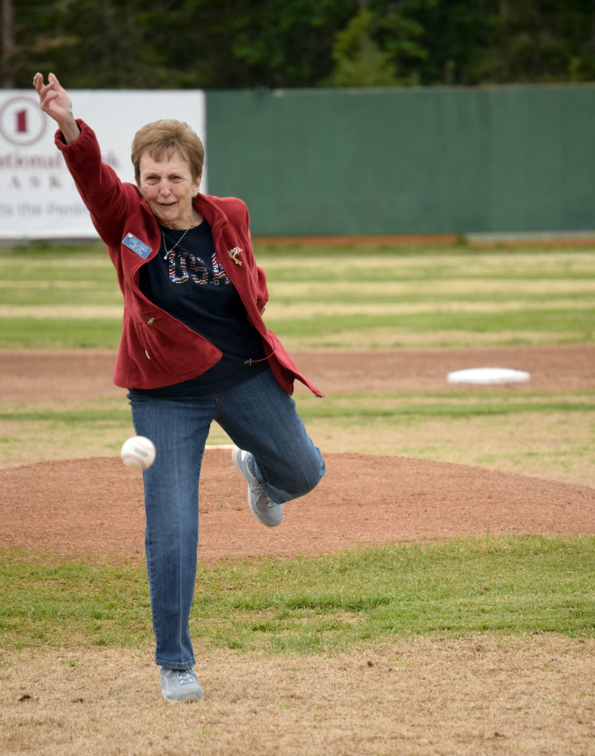 Nikiski’s Sue Coup throws out the first pitch at a ceremony honoring former Twins head coach and general manager Lance Coz on Saturday at Coral Seymour Memorial Park in Kenai. (Photo by Jeff Helminiak/Peninsula Clarion)