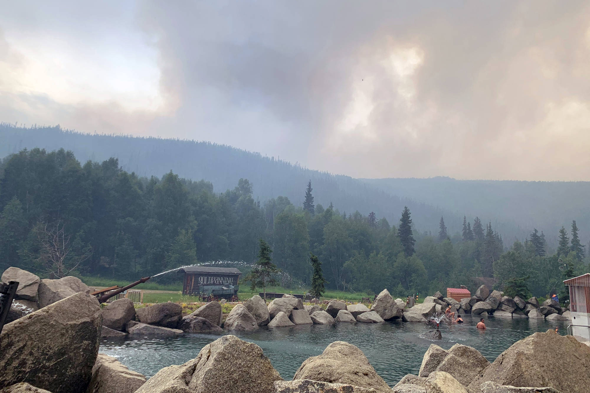 Alaska Division of Forestry via Associated Press
Smoke from the Munson Creek Fire rises behind the Chena Hot Springs Resort as guests watch from the outdoor rock pool near Fairbanks, on Monday. Authorities on Monday advised residents and guests to evacuate immediately after a nearby wildfire intensified. The Fairbanks North Star Borough issued the evacuation order when the fire reached a point less than a mile behind Chena Hot Springs.