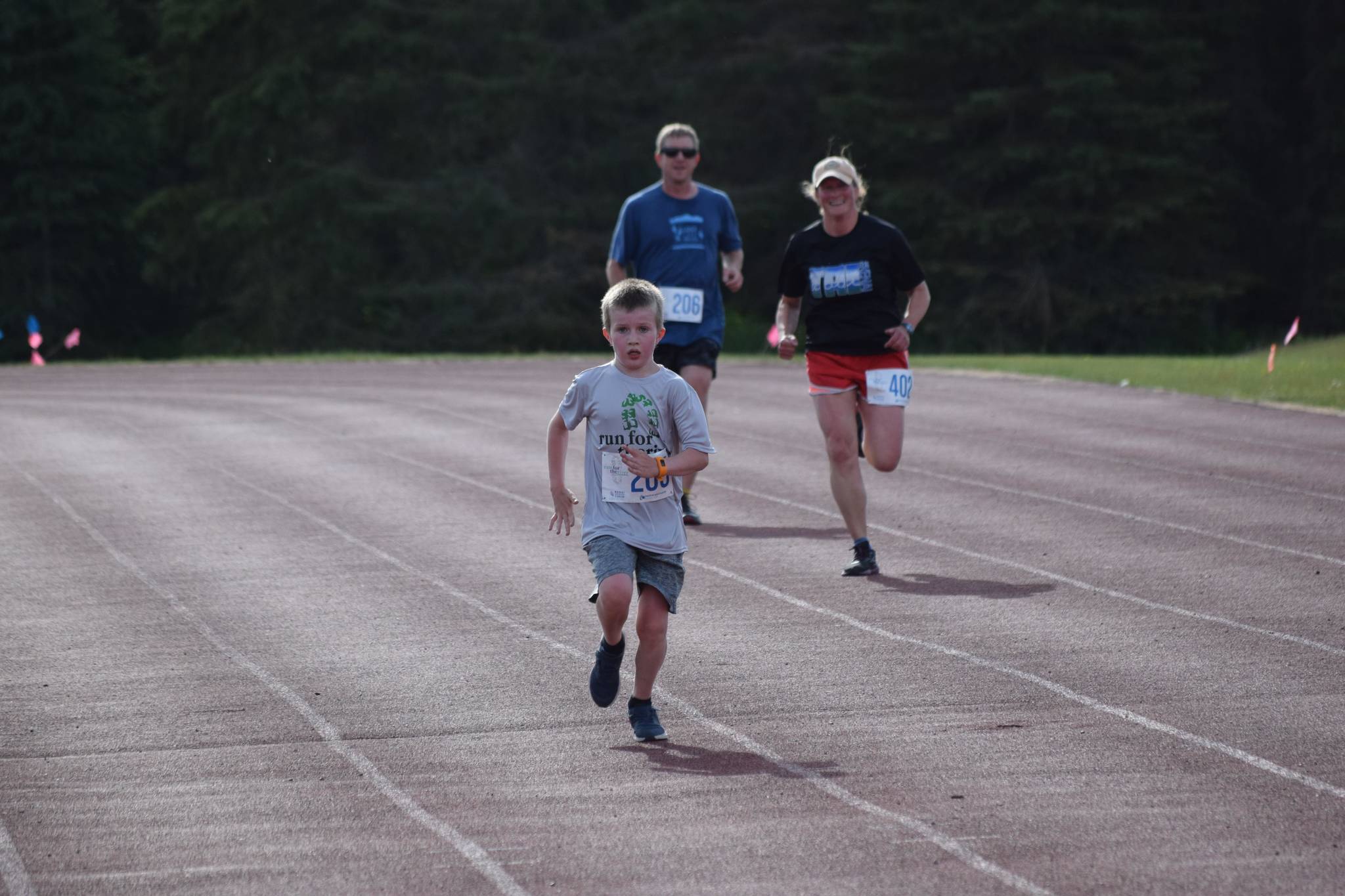 Gus Reimer crosses the finish line in front of Adam Reimer and Julie Laker during the first race of the Salmon Run Series at Skyview Middle School on Wednesday, July 7, 2021. (Camille Botello / Peninsula Clarion)