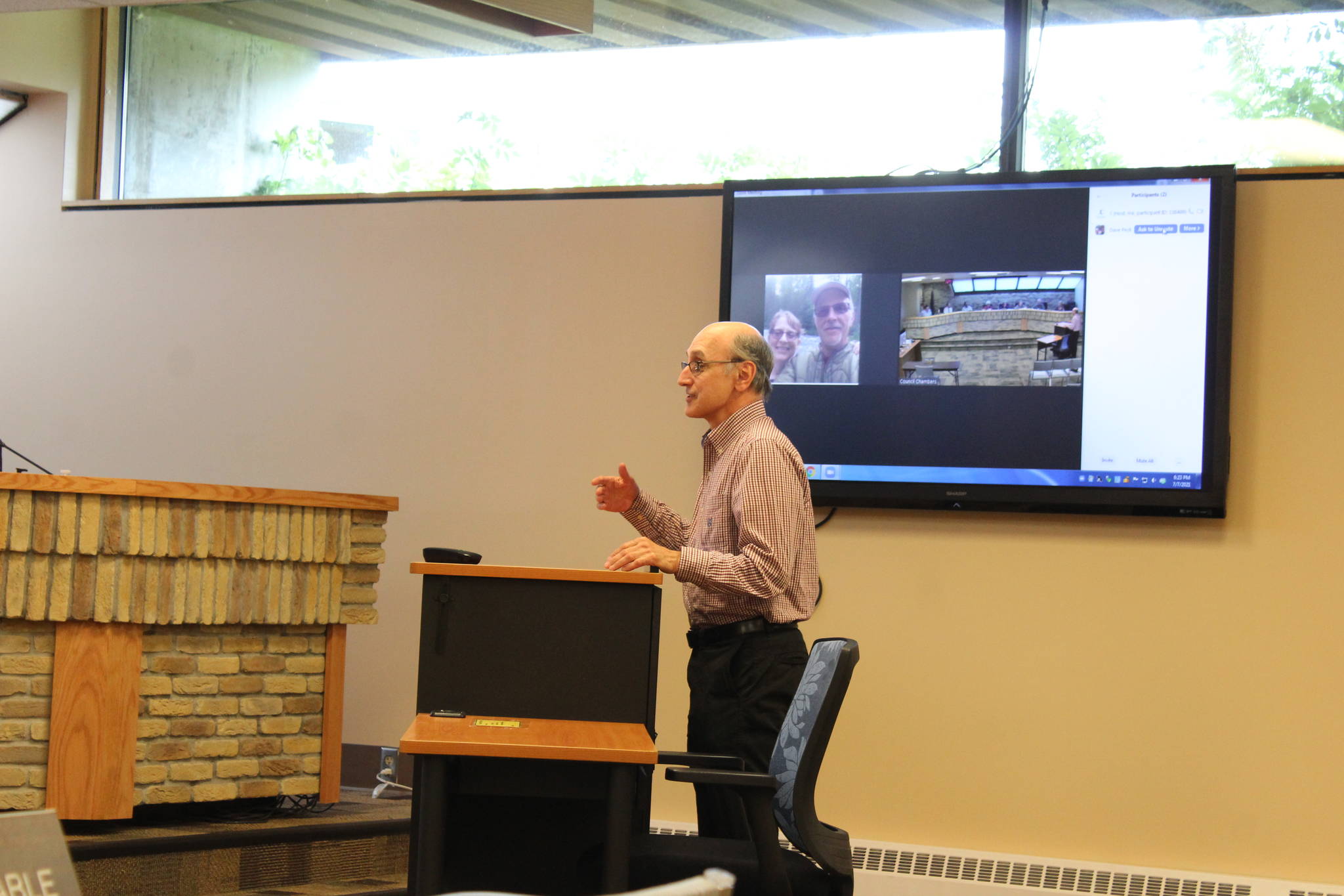 A Zoom teleconference screen can be seen behind Joe Rizzo, Triumvirate Theatre president, as he speaks to the Kenai City Council, on Wednesday, July 7, 2021, in Kenai, Alaska. The council agreed last week to continue offering Zoom services during meetings. (Photo by Ashlyn O’Hara/Peninsula Clarion)