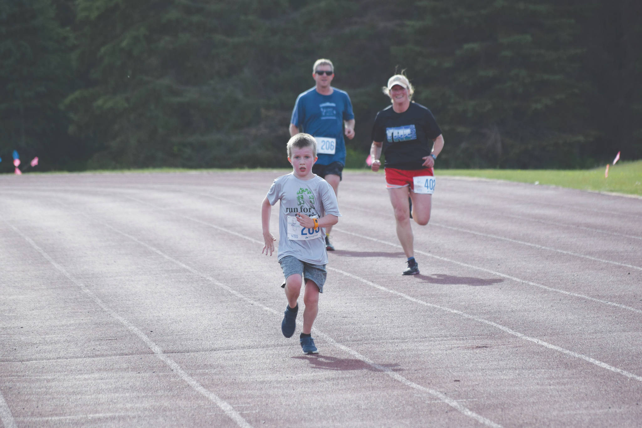 Gus Reimer crosses the finish line in front of Adam Reimer and Julie Laker during the first race of the Salmon Run Series at Skyview Middle School on Wednesday, July 7, 2021. (Camille Botello / Peninsula Clarion)