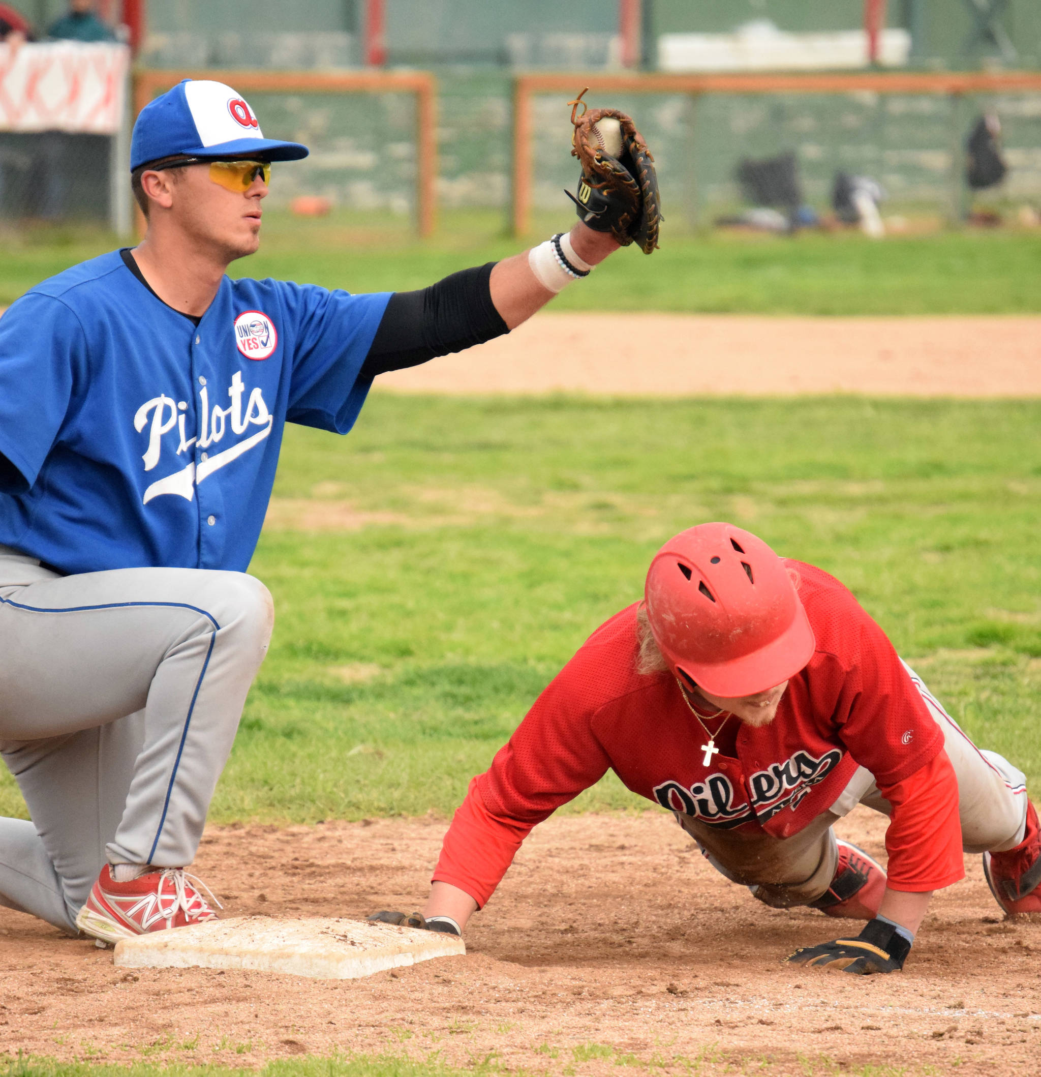 Cole Moore of the Peninsula Oilers dives into first base safely ahead of the tag of Anchorage Glacier Pilots first baseman CJ Breen on Friday, July 23, 2021, at Coral Seymour Memorial Park in Kenai, Alaska. (Photo by Jeff Helminiak/Peninsula Clarion)