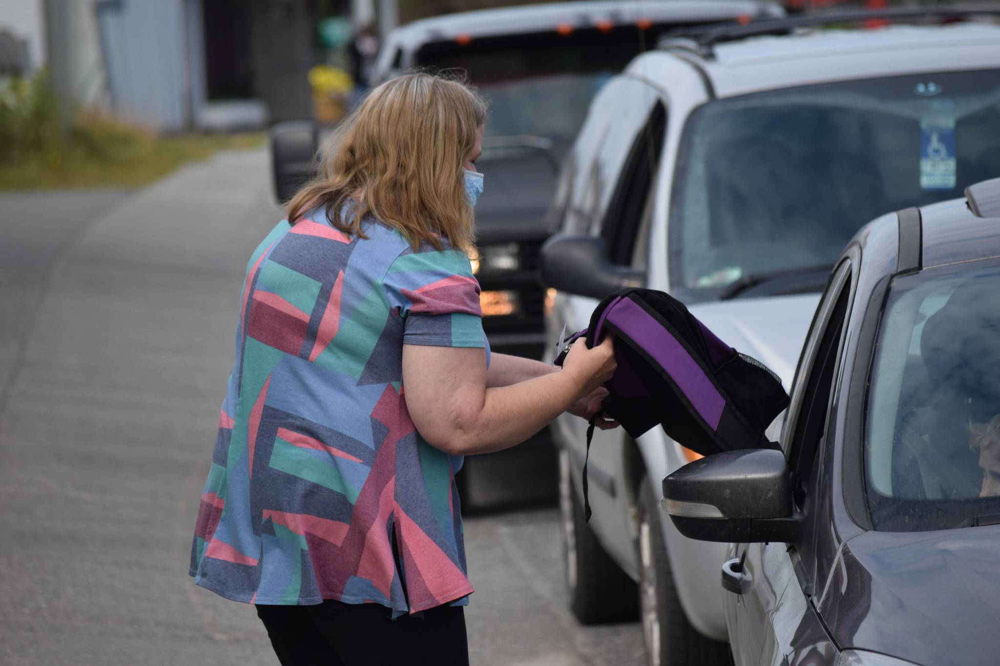 Joanne Jenkins distributes backpacks and school supplies to a line of cars at the Peninsula Community Health Services KidFest event on Wednesday, Aug. 4, 2021 in Kenai, Alaska. (Camille Botello/Peninsula Clarion)