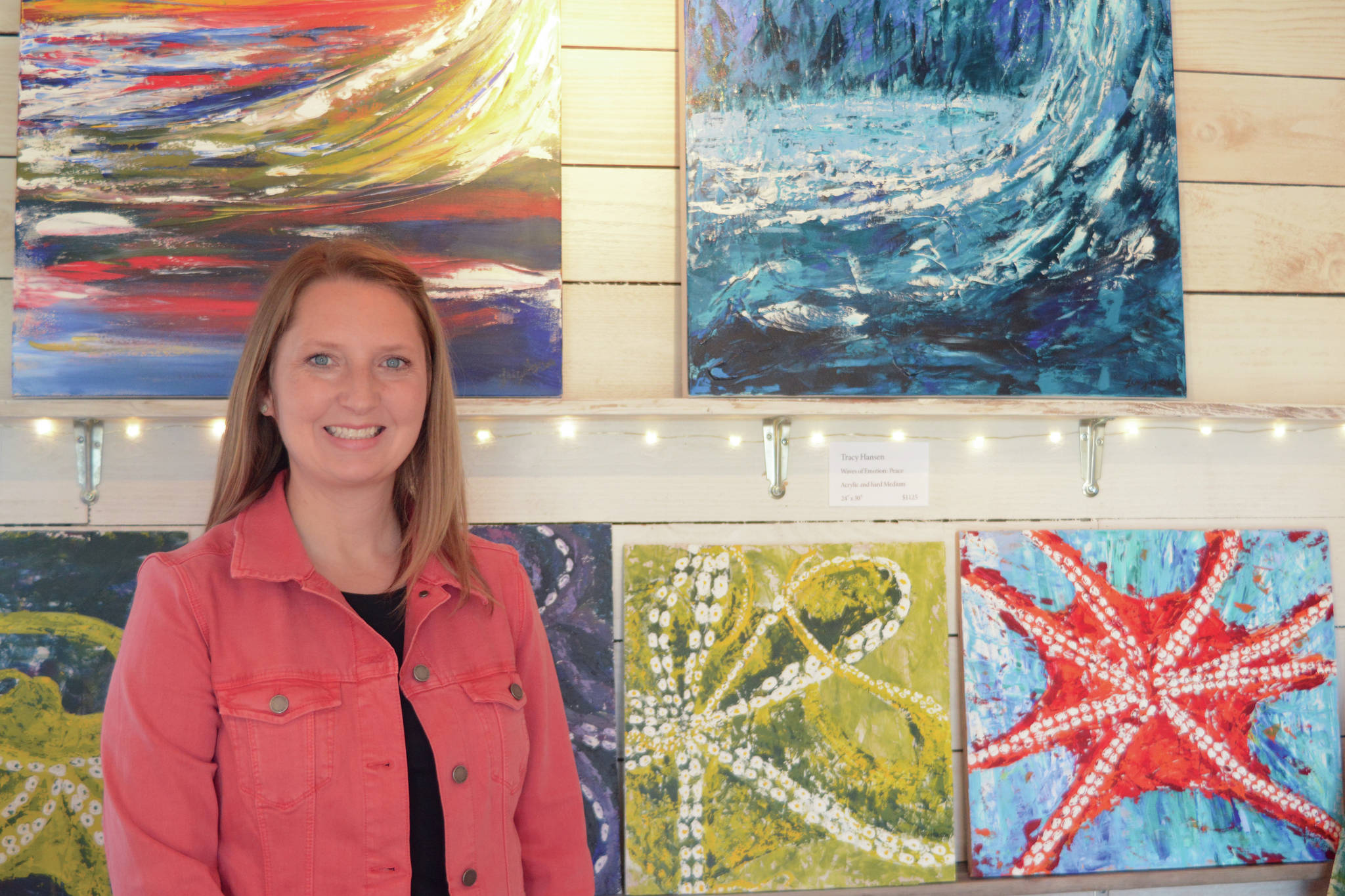 Tracy Hansen poses for a photo in front of her paintings at her Ocean Drive shop, 59 North, on Tuesday, Aug. 10, 2021, in Homer, Alaska. (Photo by Michael Armstrong/Homer News)