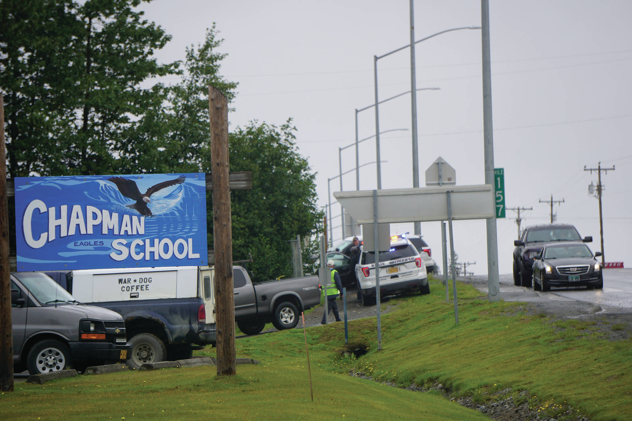 Parents on Monday, Aug. 23, 2021, pick up students at Chapman School in Anchor Point, Alaska, after a shooting about a half mile north on the Sterling Highway in which an Alaska State Trooper was shot. The school was on lockdown while troopers searched for the alleged shooter, Bret Herrick, 60. An Alaska State Trooper stands by. (Photo by Michael Armstrong/Homer News)