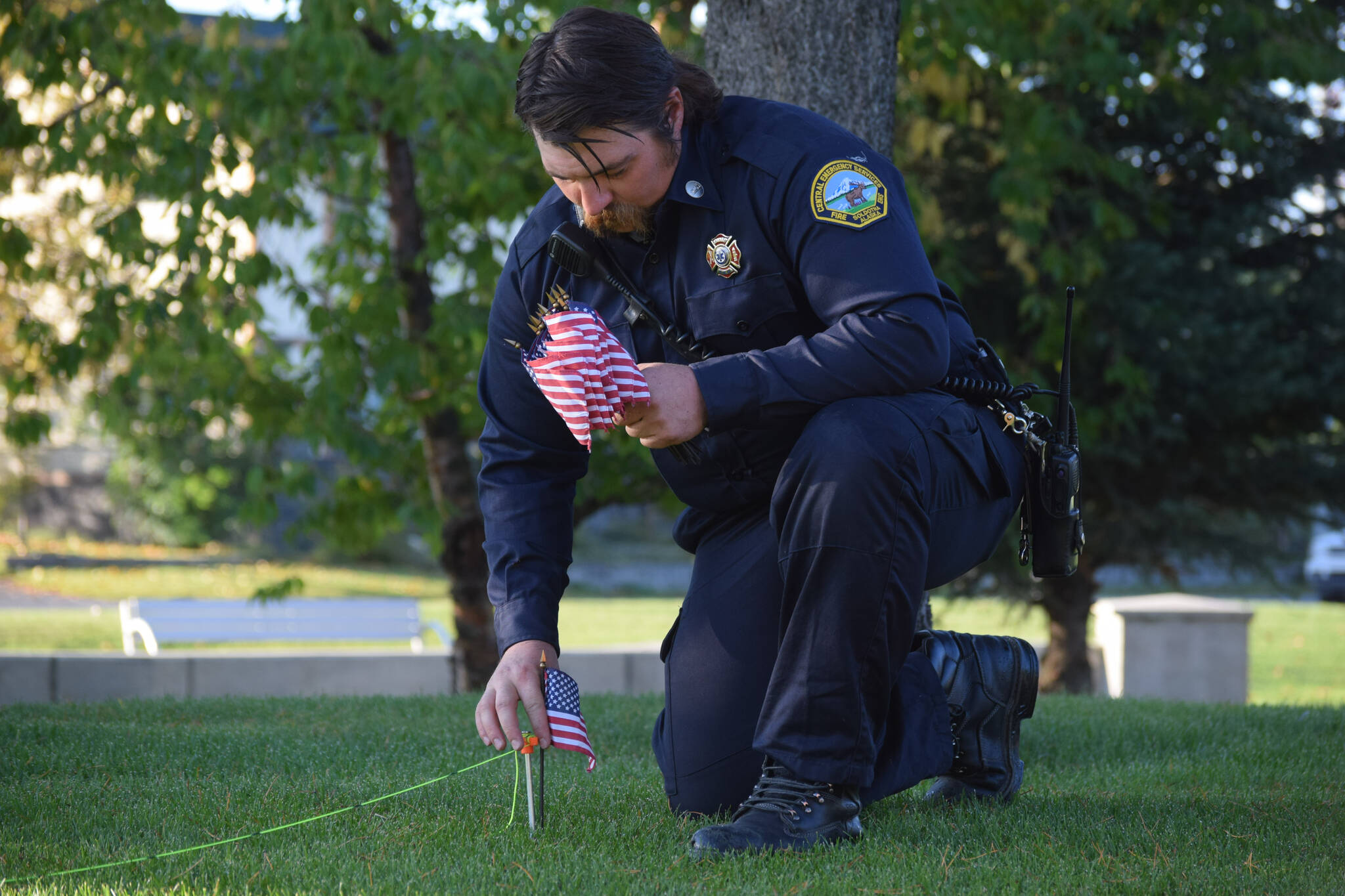 A firefighter with Central Emergency Services in Soldotna places an American flag in front of the station. Firefighters set over 400 flags in the grass outside CES in Soldotna on Saturday, Sept. 11, 2021 in honor of the first responders who died in the 9/11 terrorist attacks. (Camille Botello/Peninsula Clarion)