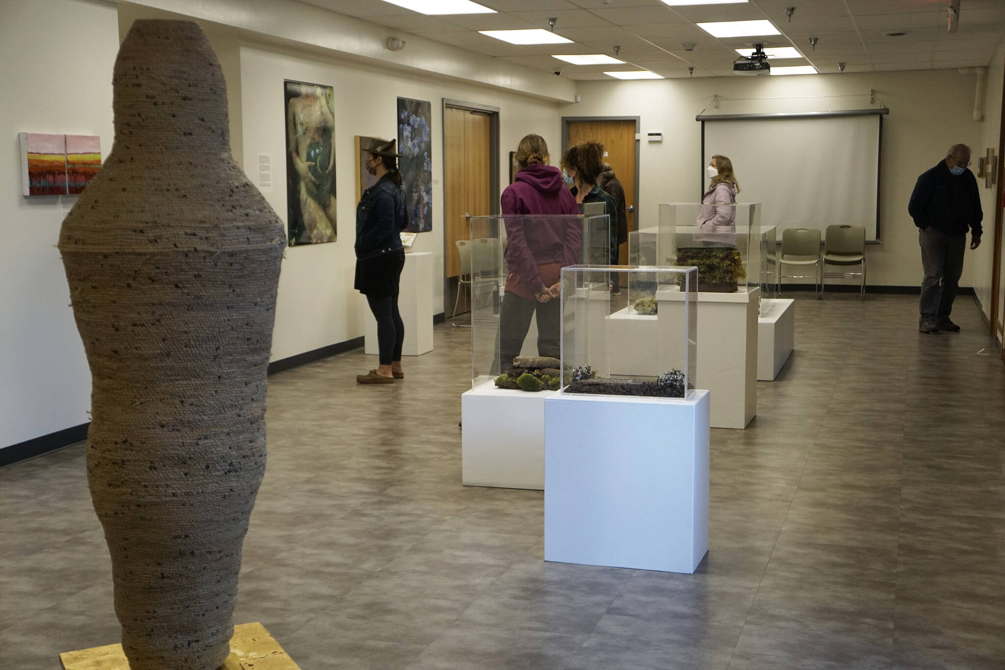 People visit the Homer Drawdown Peatland exhibit last Friday, Sept. 17, 2021, at a reception and talk at the Pratt Museum & Park in Homer, Alaska. At left is Sheryl Maree Reily’s “Sarcophagus.” (Photo by Michael Armstrong/Homer News)