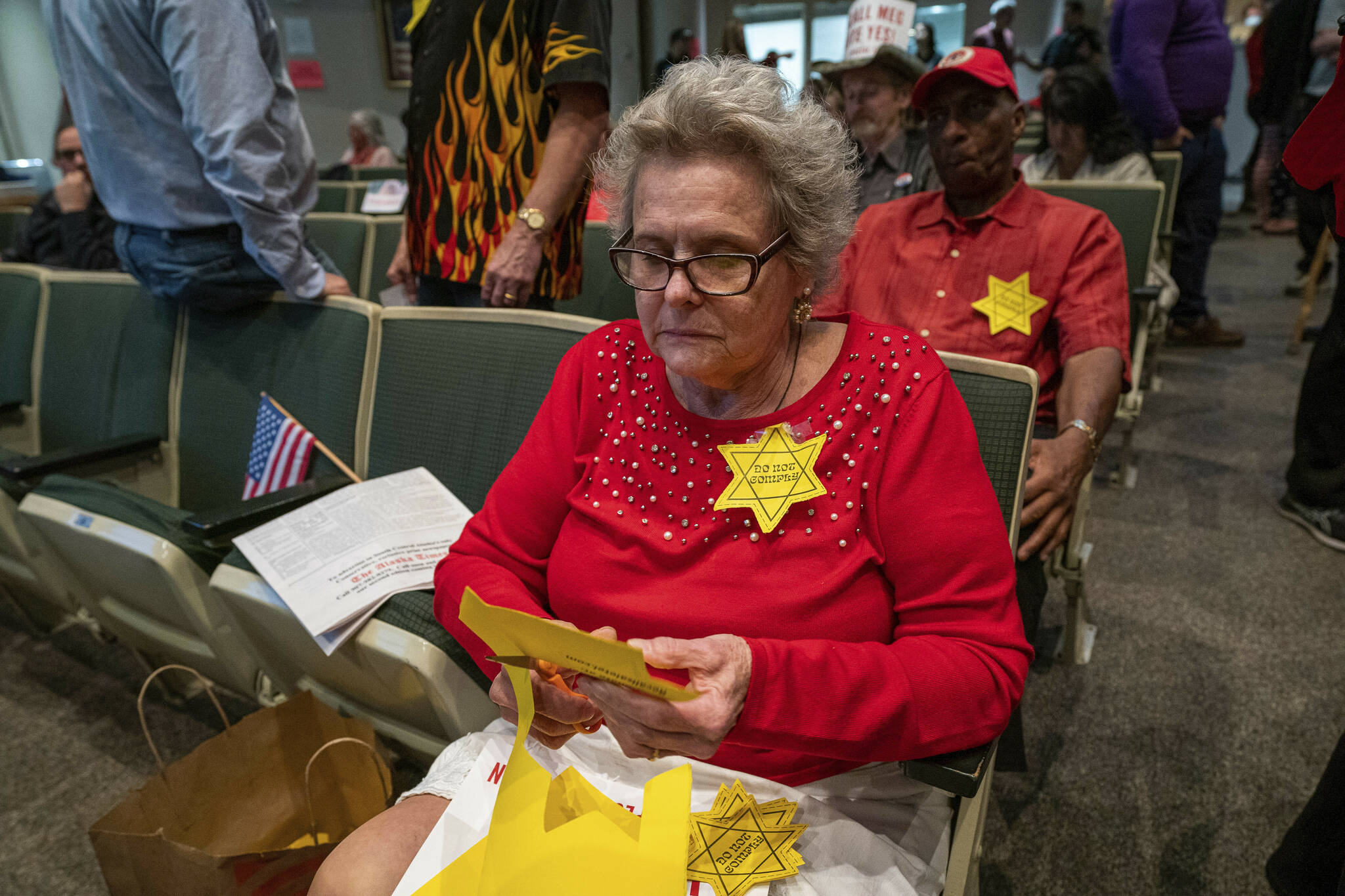 Christine Hill cuts out yellow Stars of David before an Anchorage Assembly meeting where the body heard public testimony from people about a proposed mask mandate on Wednesday in Anchorage. Hill, who is opposed to a mask mandate, had printed out the stars at home and was handing them out for others to wear during the meeting. She said she wore a star as a comparison to the oppression and genocide of Jewish people in Nazi Germany. Anchorage Mayor Dave Bronson apologized Thursday, Sept. 30, 2021, for his comments supporting some residents’ use of Holocaust imagery to liken a proposed citywide mask mandate to the oppression of Jewish people in Nazi Germany. (Loren Holmes/Anchorage Daily News via AP)