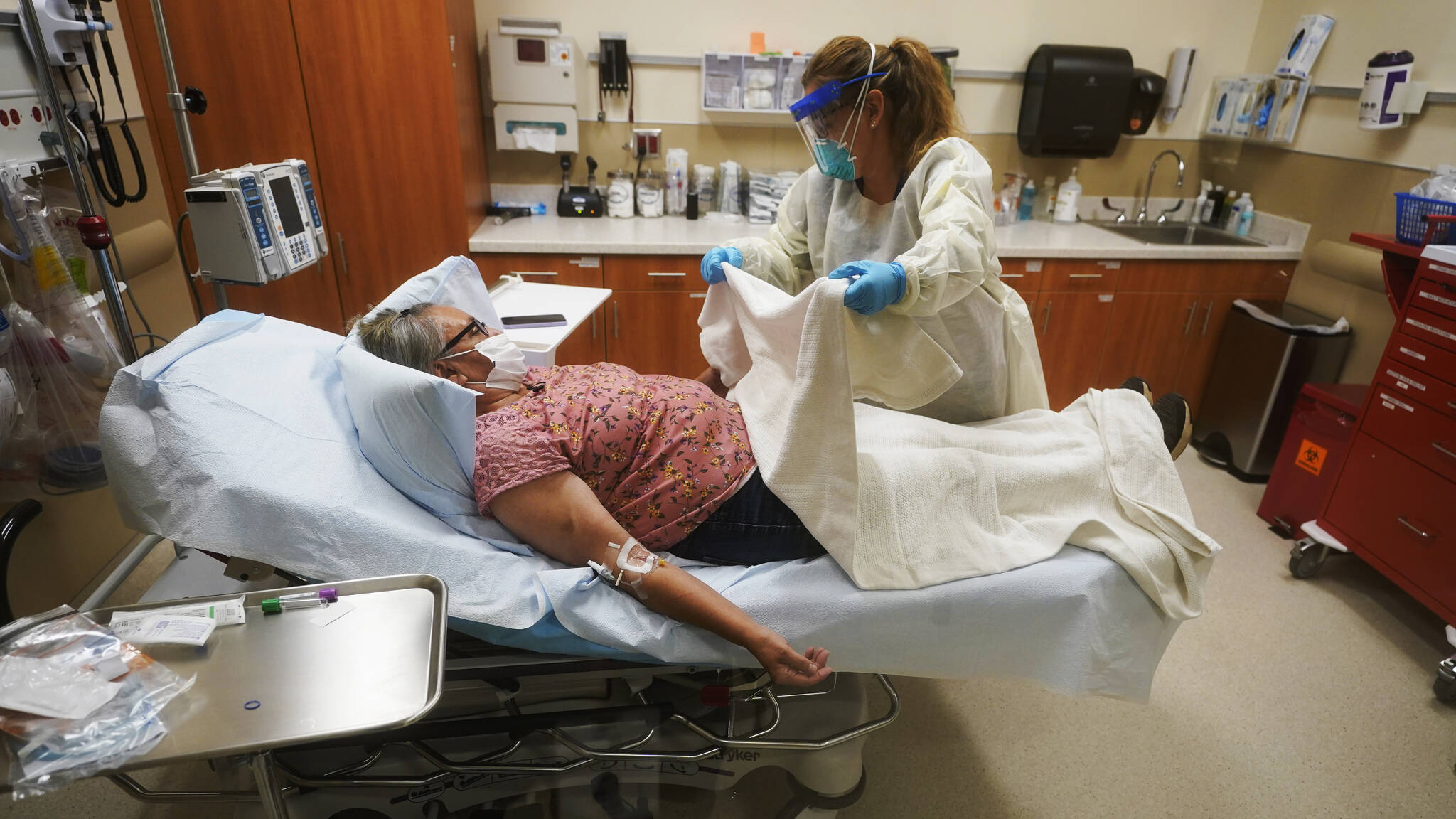 Angie Cleary, a registered nurse, cares for Joyce Johnson-Albert as she receives an antibody infusion while lying on a bed in a trauma room at the Upper Tanana Health Center Wednesday, Sept. 22, 2021, in Tok, Alaska. Johnson-Albert was optimistic but also realistic. “I just hope the next few days I’ll be getting a little better than now,” Johnson-Albert told a reporter on the other side of a closed, sliding glass door to the treatment room two days after testing positive for COVID-19 and while receiving an antibody infusion. “It’s just hard to say. You can go either way.” (AP Photo/Rick Bowmer)