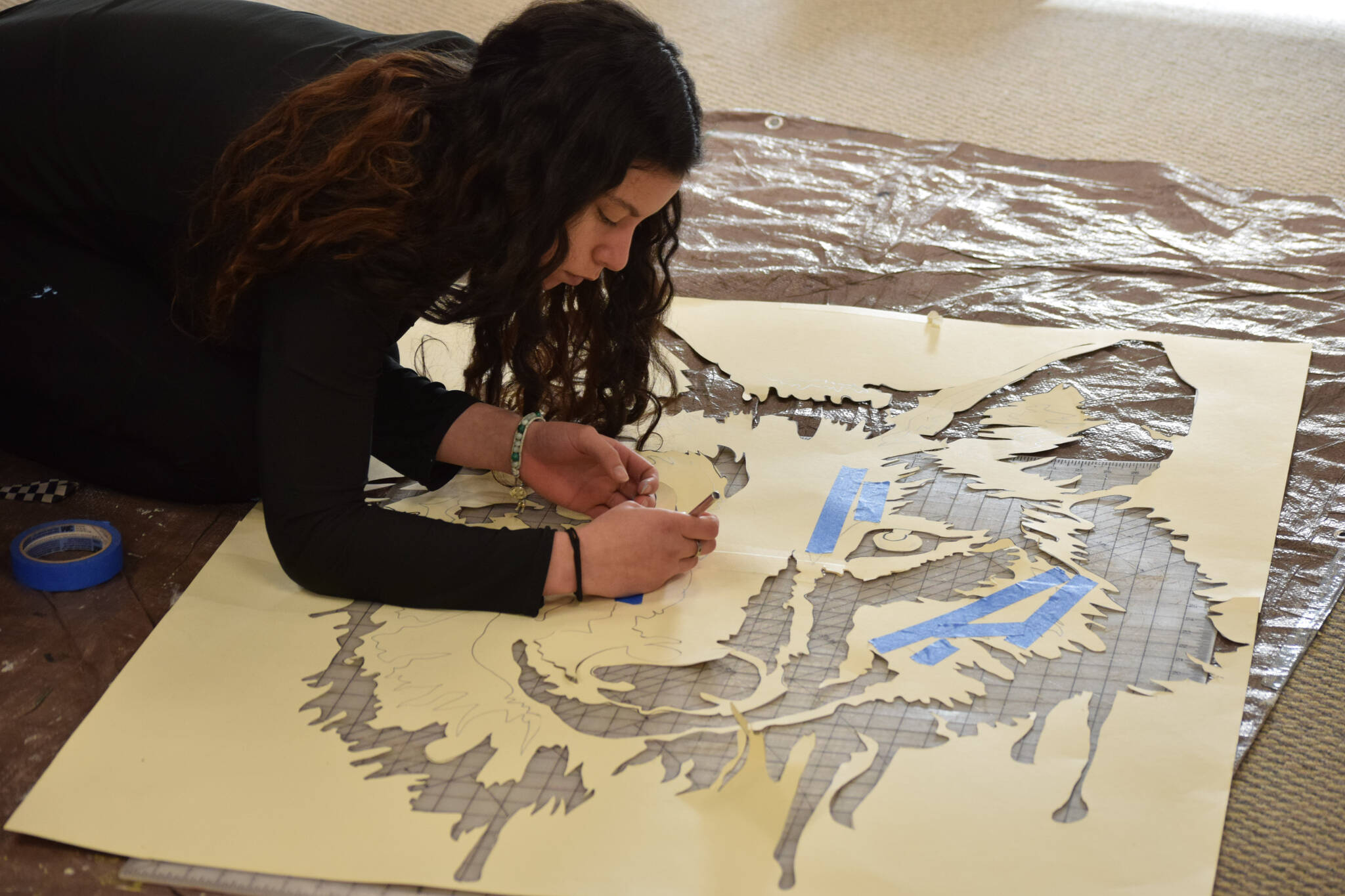 Tatihana DeHoyos cuts out the centerpiece stencil for the Kenai Alternative High School’s mural installation at the Kenai Art Center on Tuesday, Nov. 9, 2021. (Camille Botello/Peninsula Clarion)
