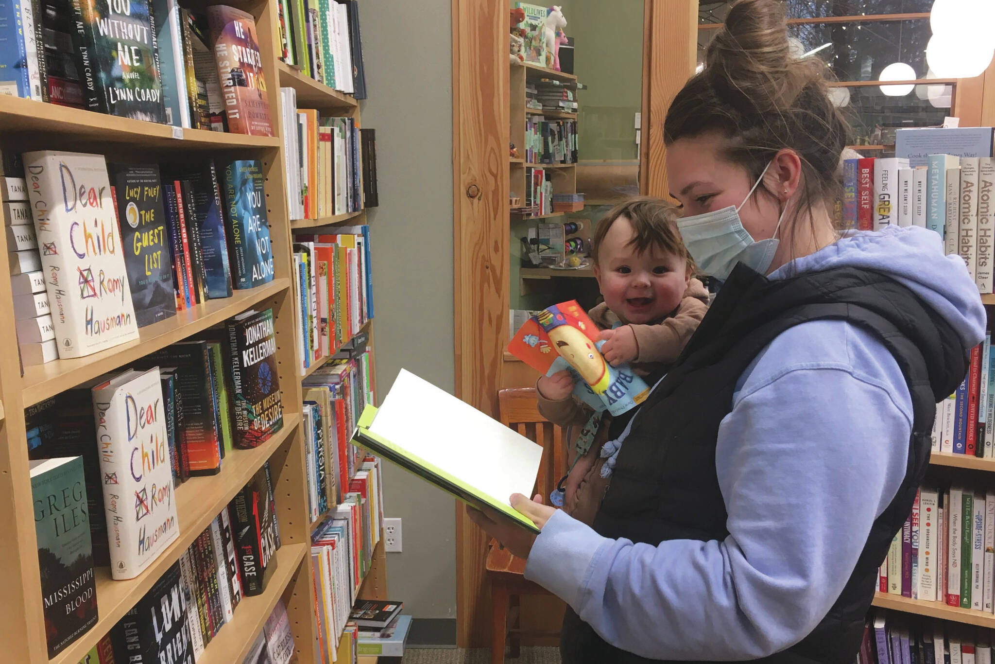 Jessie Duke, of Soldotna, browses books with 7-month-old Danny Dommek on Monday, Nov. 16, 2020, at River City Books in Soldotna, Alaska. River City Books participated in the 2020 shop local program in Soldotna. The city is bringing the program back for a second time this holiday season. (Photo by Jeff Helminiak/Peninsula Clarion)