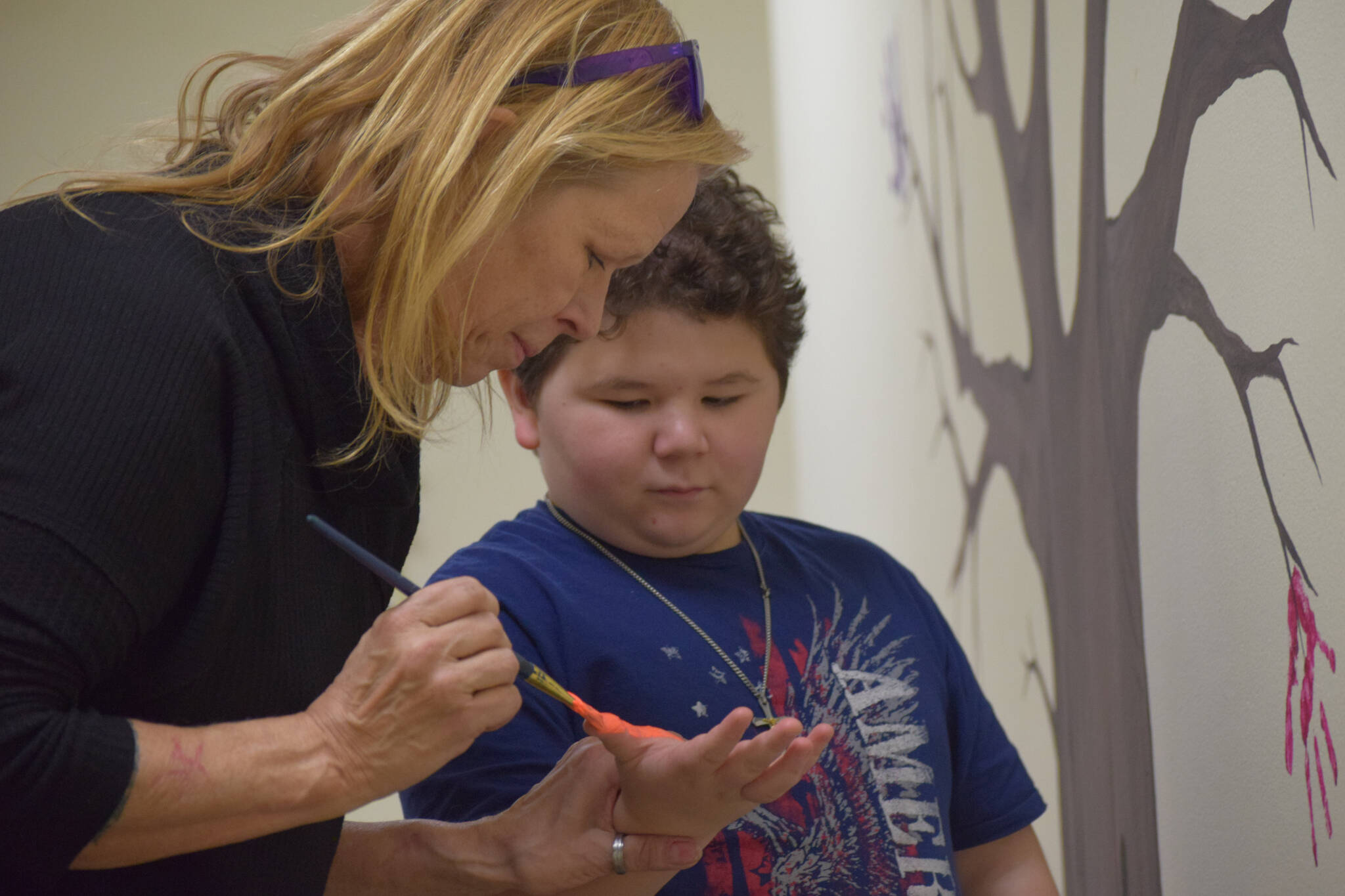 Carolyn Massey paints 10-year-old Kenny Smith’s hand to add to the helping hands tree at the Children’s Advocacy Center on Tuesday, Nov. 16, 2021, in Kenai, Alaska. (Camille Botello/Peninsula Clarion)