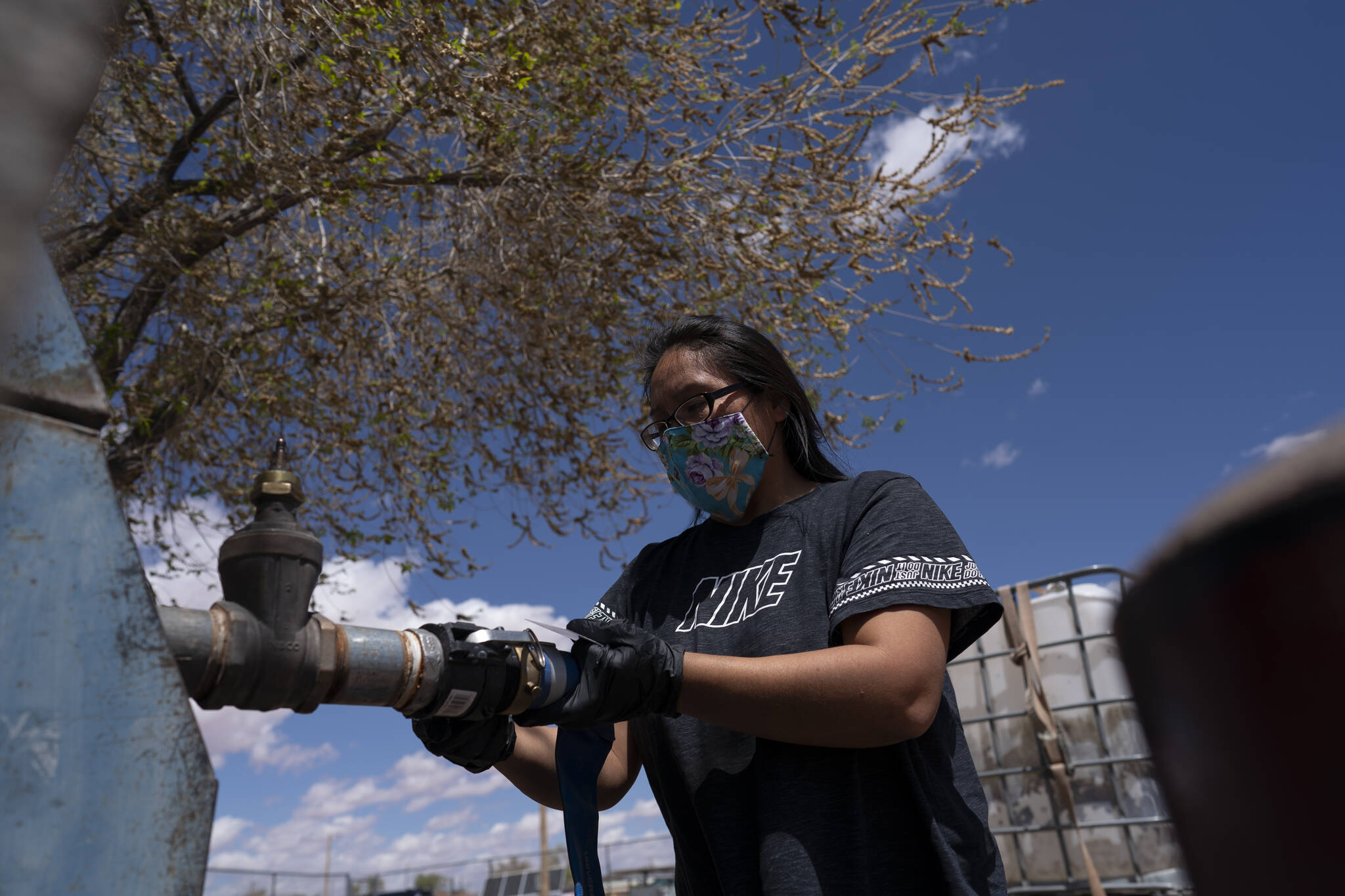 Raynelle Hoskie attaches a hose to a water pump to fill tanks in her truck outside a tribal office on the Navajo reservation in Tuba City, Ariz., on April 20, 2020. A massive infrastructure bill that President Joe Biden signed this week includes billions of dollars to address long-standing issues with water and sanitation on tribal land. (AP Photo/Carolyn Kaster, File)