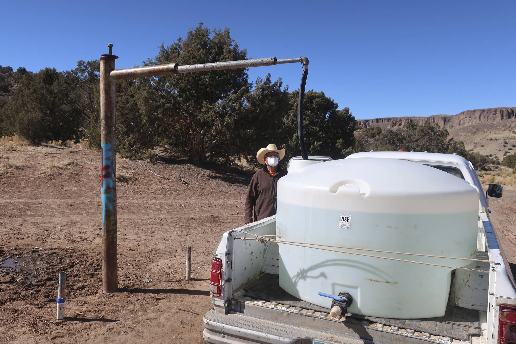 Phillip Yazzie waits for a water drum in the back of his pickup truck to be filled in Teesto, Ariz., on the Navajo Nation, on Feb. 11, 2021. A massive infrastructure bill that President Joe Biden signed this week includes billions of dollars to address long-standing issues with water and sanitation on tribal land. (AP Photo/Felicia Fonseca, File)