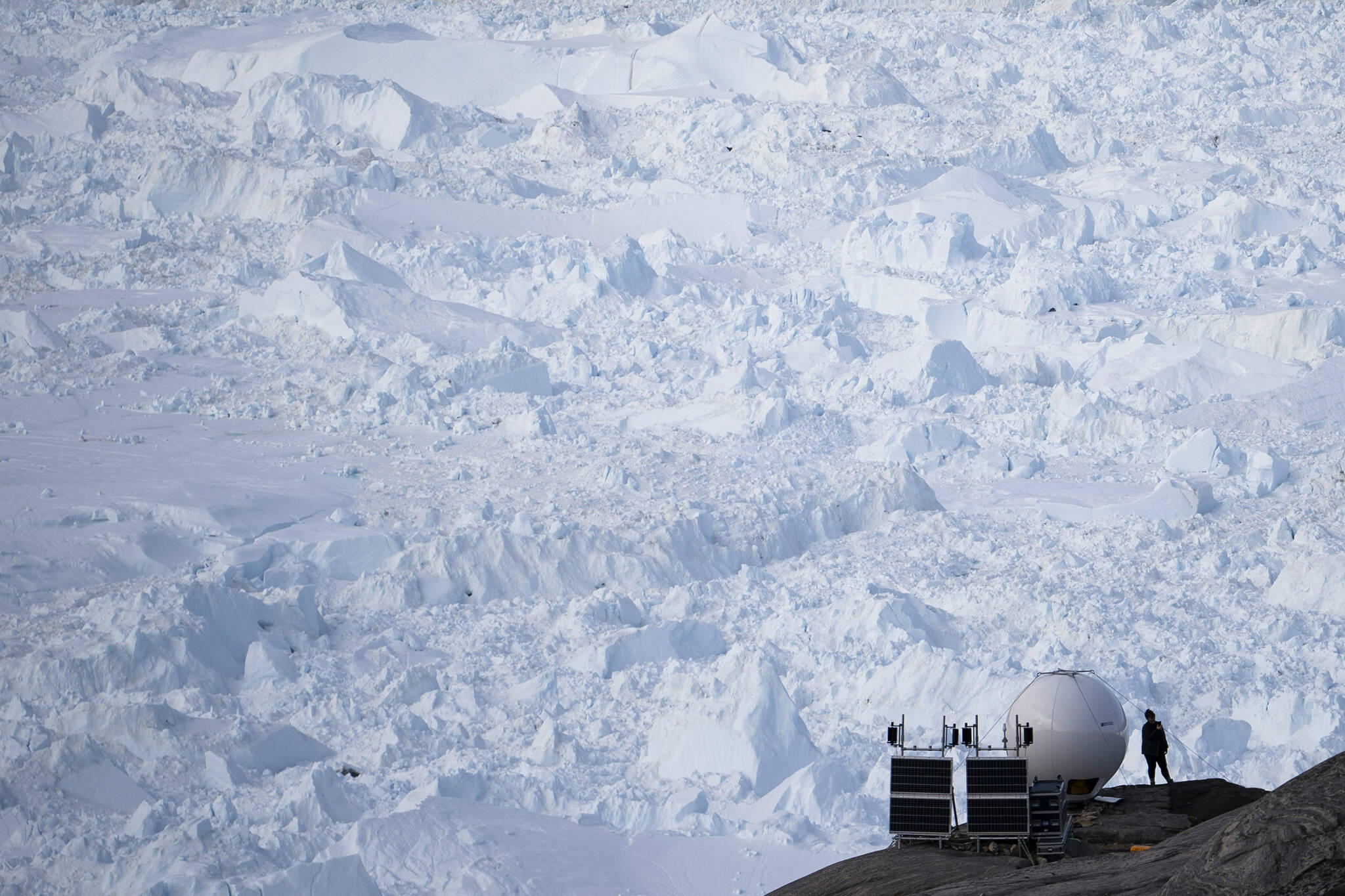 A woman stands next to an antenna at an NYU base camp at the Helheim glacier in Greenland on Friday, Aug. 16, 2019. In an effort to combat climate change and help develop Arctic communities, the Department of Energy Wednesday announced it was seeking to develop new sustainable energy projects in Alaska. (AP Photo / Felipe Dana)