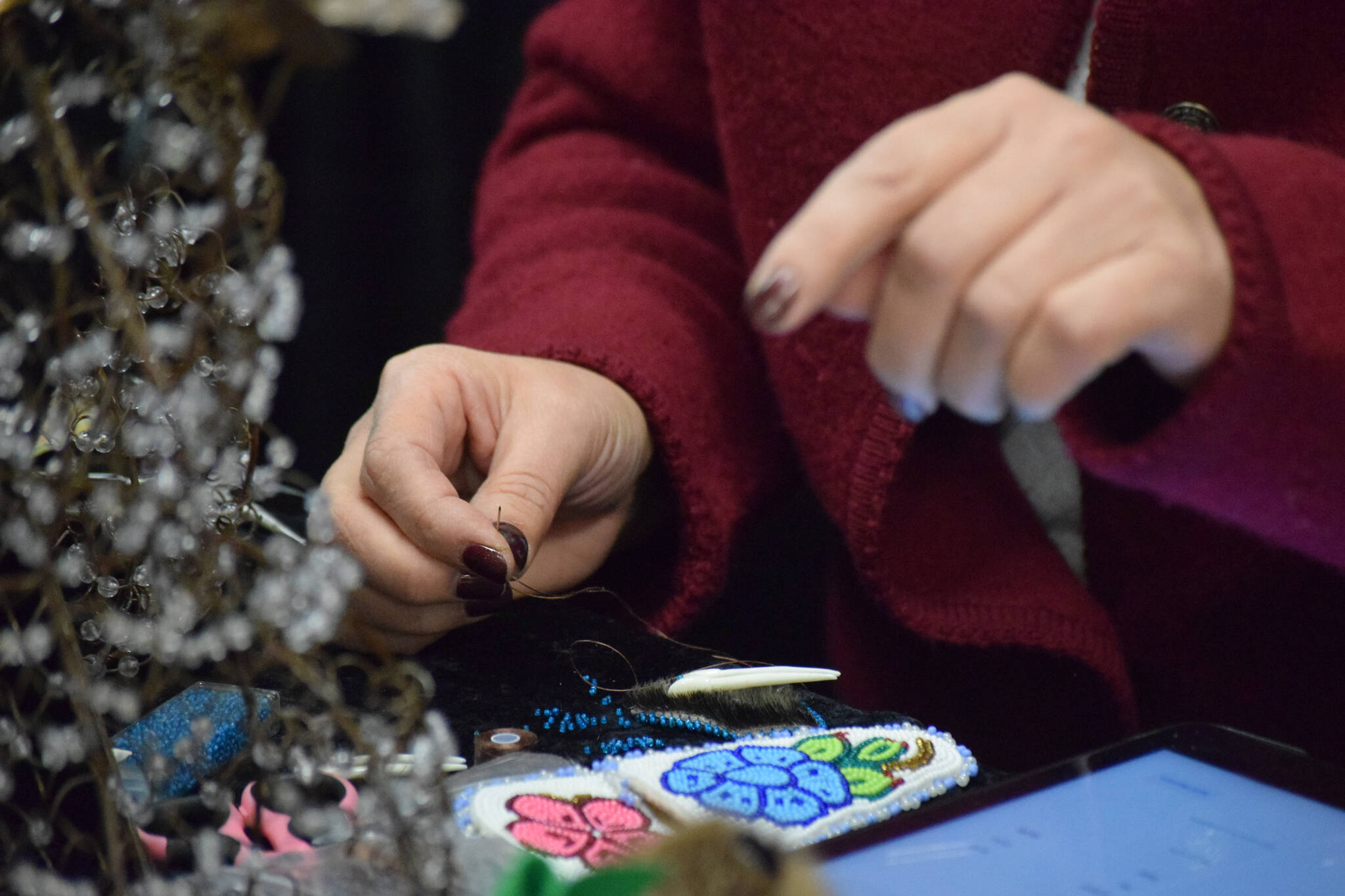 Michelle Ravenmoon sews a beaded artisan product at the Soldotna Holiday Bazaar at the Soldotna Regional Sports Complex on Saturday, Nov. 20, 2021. (Camille Botello/Peninsula Clarion)
