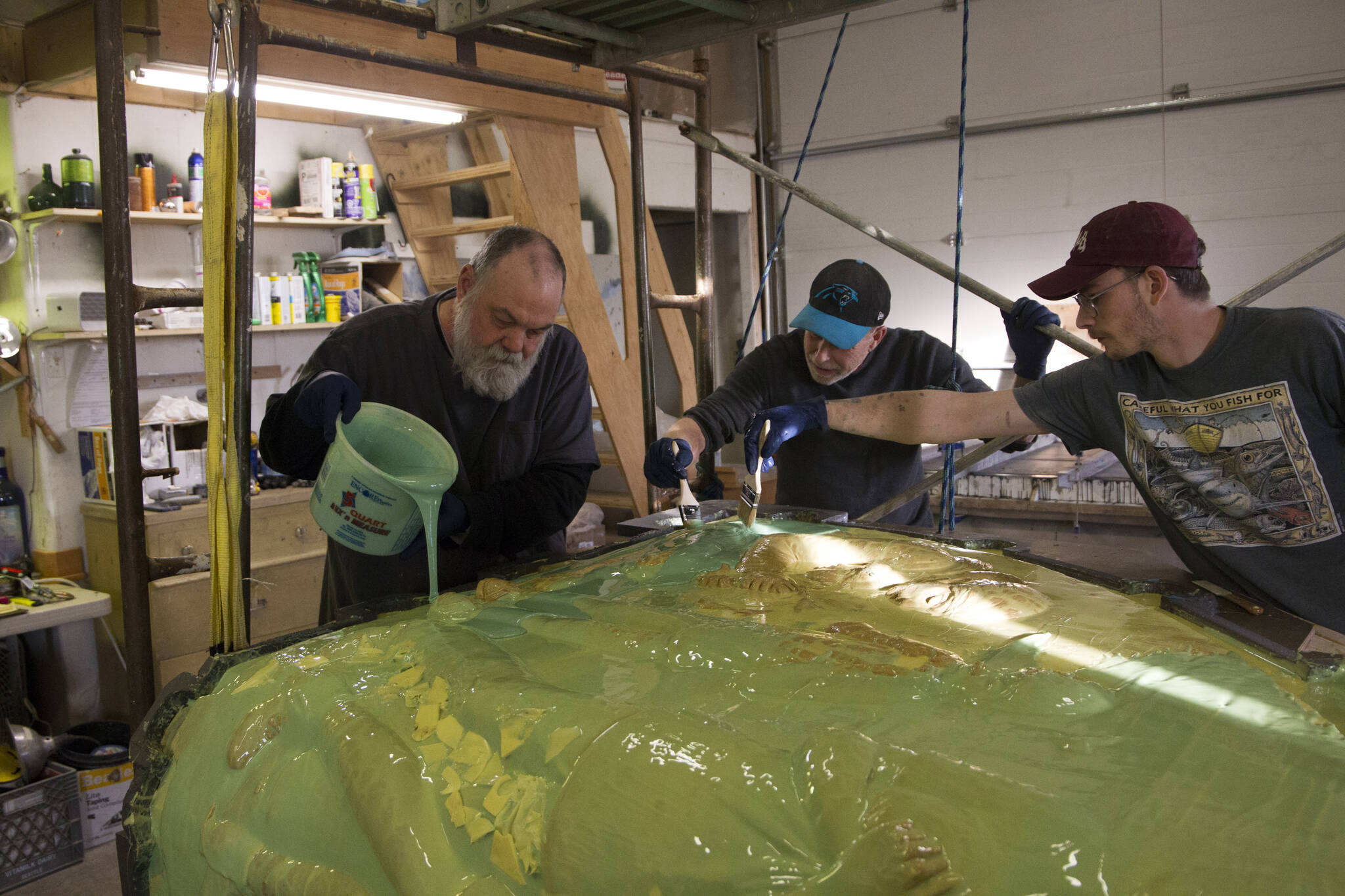 Bench creator, Brad Hughes, pours the molding material over the clay while Rob Wiard and Matt brush the liquid rubber over each character on the bench to ensure it is covered evenly. (Photo by Sarah Knapp/Homer News)