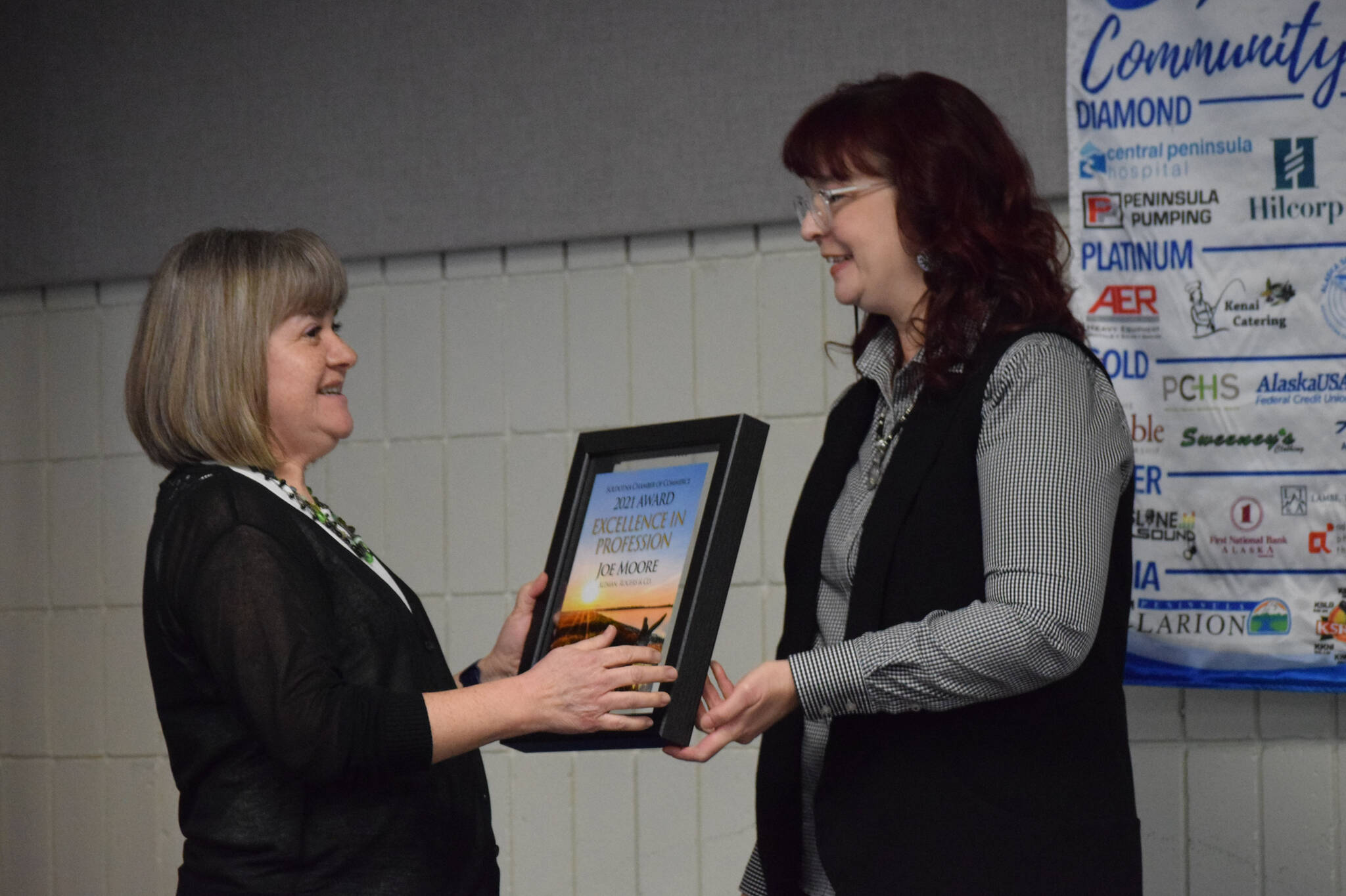 Monica Frost accepts the Soldotna Chamber of Commerce’s Excellence in profession award from Sara Hondel on behalf of Joe Moore of the Altman, Rogers Co. certified public accounting firm, during the chamber’s 2021 award ceremony at the Soldotna Sports Complex on Wednesday, Feb. 9, 2022. (Camille Botello/Peninsula Clarion)