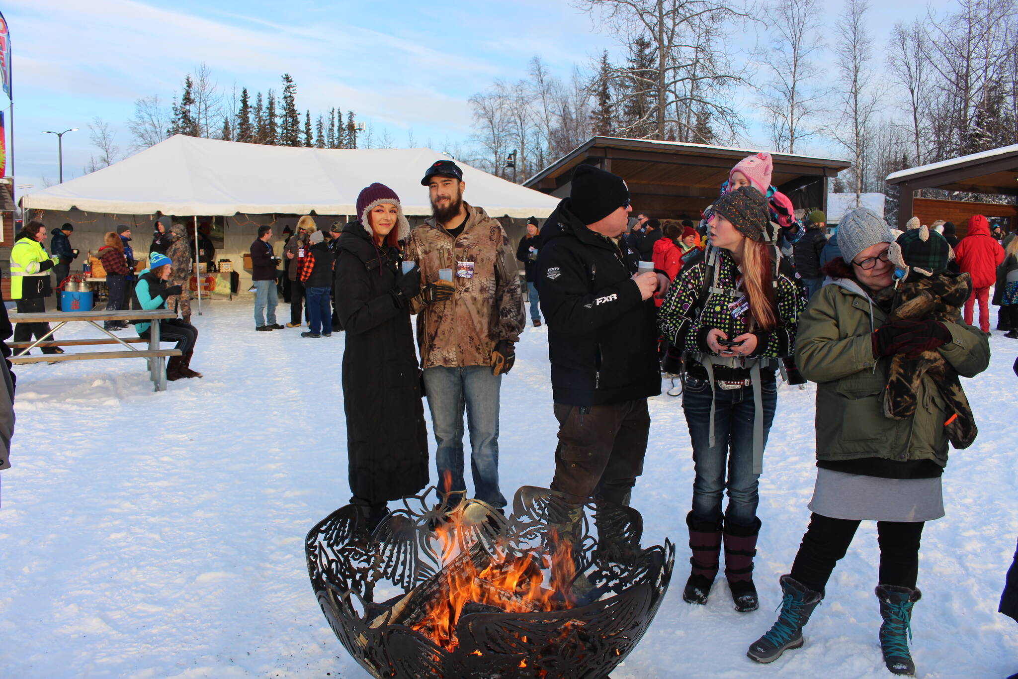 From left, Tiana McGahan, Aaron Hughes, Victor Thompson, McKayla Chadburn and Dawn Rimer keep warm around the fire during the 2020 Frozen RiverFest at Soldotna Creek Park in Soldotna, Alaska on Feb. 15, 2020. (Photo by Brian Mazurek/Peninsula Clarion)