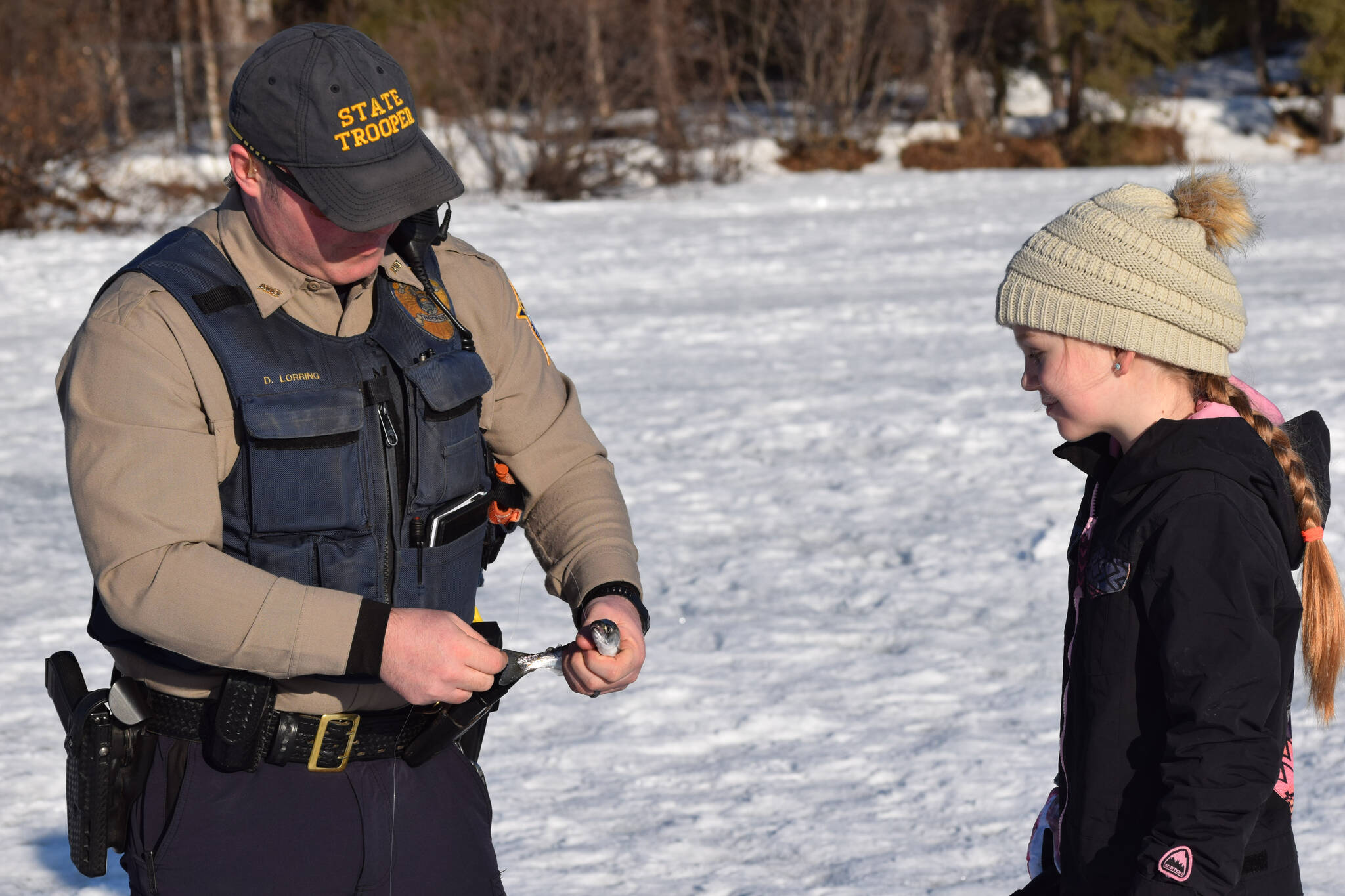 David Lorring, left, helps Moriah Hodges, right, reel in her fish at Sport Lake in Soldotna as part of the Alaska Department of Fish and Game’s “Salmon in the Classroom” ice fishing educational program on Wednesday, March 2, 2022, in Soldotna, Alaska. (Camille Botello/Peninsula Clarion)