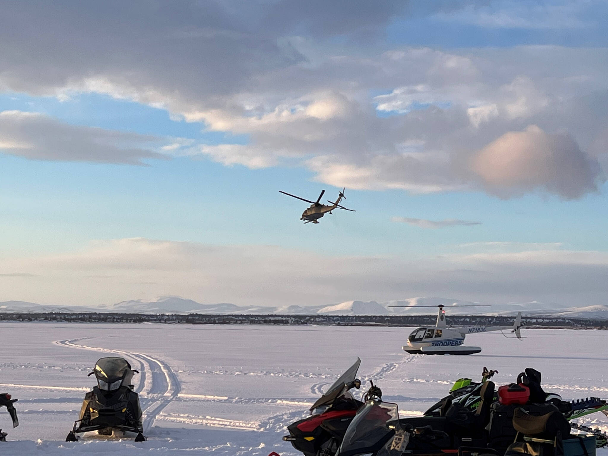 In this photo provided by Alaska State Troopers, snowmobiles and a plane that responded to provide assistance are seen gathered on a frozen lake in southwest Alaska that was the site of a small plane crash on Saturday, March 5, 2022, near Iliamna, Alaska. Authorities say the five people on board the plane were injured. (Trooper Travis Lons/Alaska State Troopers via AP)