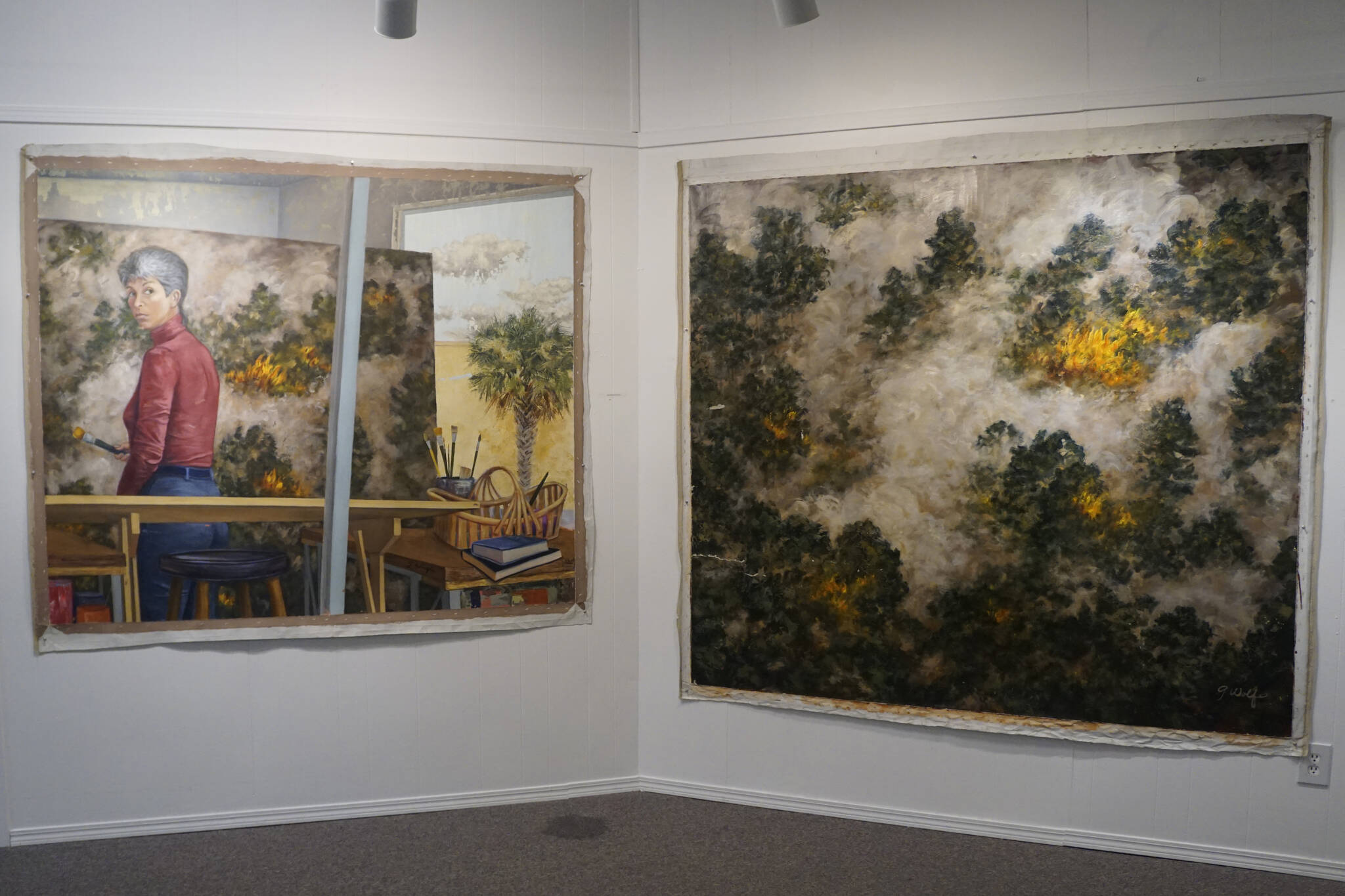 “Selected Works and Sketches by Gaye Wolfe,” showing at the Homer Council on the Arts through March, includes these two paintings by Wolfe: a painting of a wildfire, right, and then a self-portrait of Wolfe, left, creating the painting. (Photo by Michael Armstrong/Homer News)