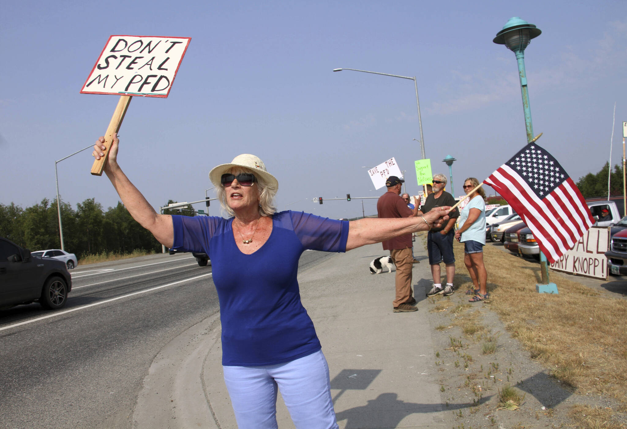 Katherine Hayes waves a flag and a sign urging Alaska lawmakers to fund a full oil wealth fund check, known locally as the PFD or Permanent Fund Dividend, Monday, July 8, 2019, in Wasilla, Alaska. Momentum is building for a constitutional convention question that will be on the ballot this year in Alaska, and similar questions will go before voters in Missouri and New Hampshire. Critics say the times are too partisan and the country is too divided to reopen state constitutions for rewriting or amendments. (AP Photo/Mark Thiessen, File)