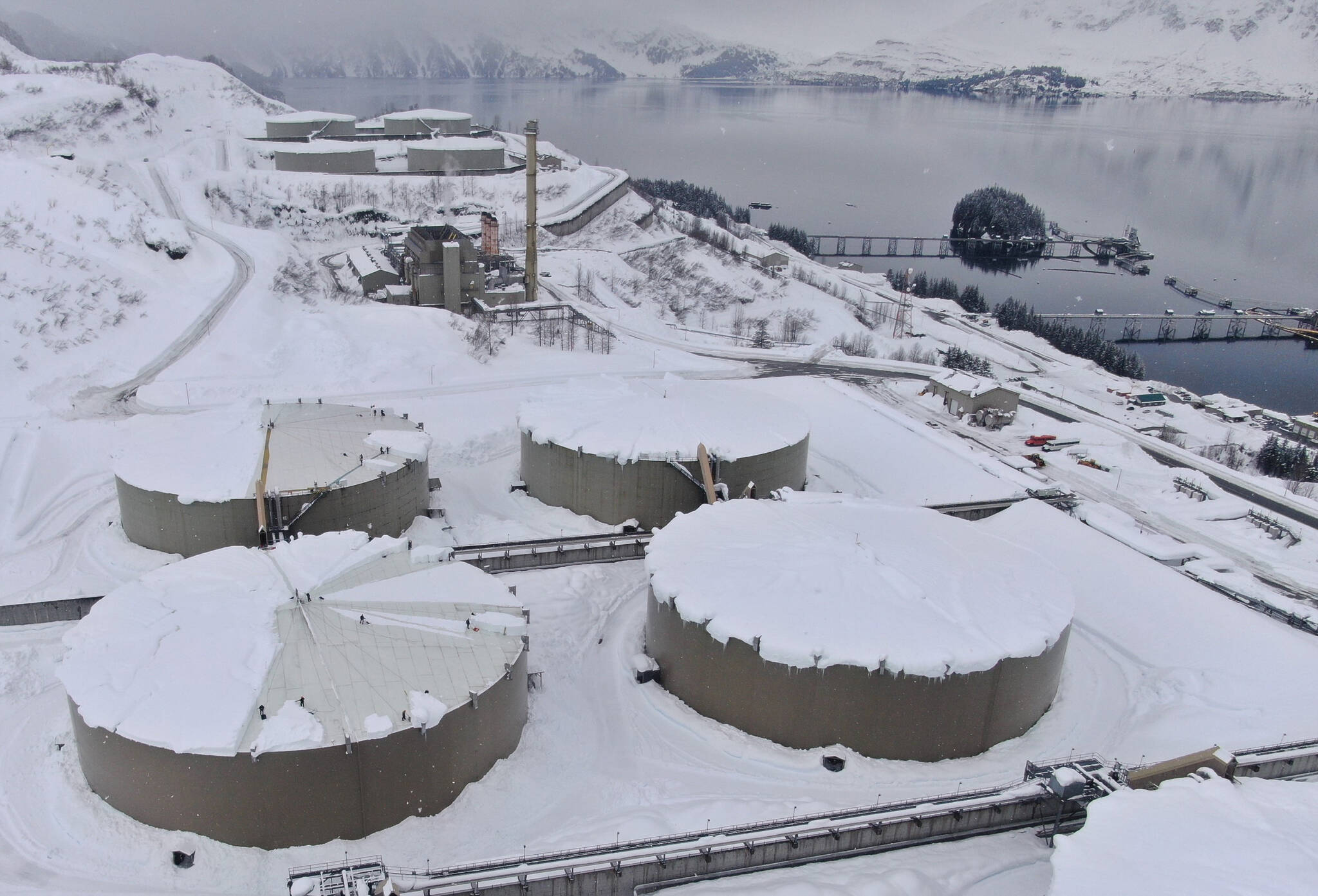 This March 16, 2022, drone photo provided by Alyeska Pipeline Co. shows snow covering 62-foot tall and acre-wide oil tanks at the Valdez Marine Terminal in Valdez, Alaska. Workers at the endpoint of the trans-Alaska oil pipeline are using saws to cut up large blocks of hard-packed snow on top of the oil storage tanks so they can shove the chunks off the tanks, some of which have damaged infrastructure after more than 4 feet of snow fell in Valdez in a month. (Alyeska Pipeline Service Company via AP)