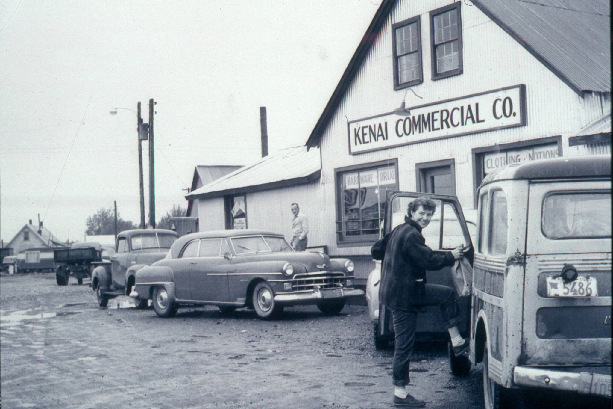 Better Homes & Gardens article photo, 1955 
Rusty Lancashire, who befriended her neighbor, Miriam Mathers, climbs into her vehicle in front of the Kenai Commercial Company store in Kenai.