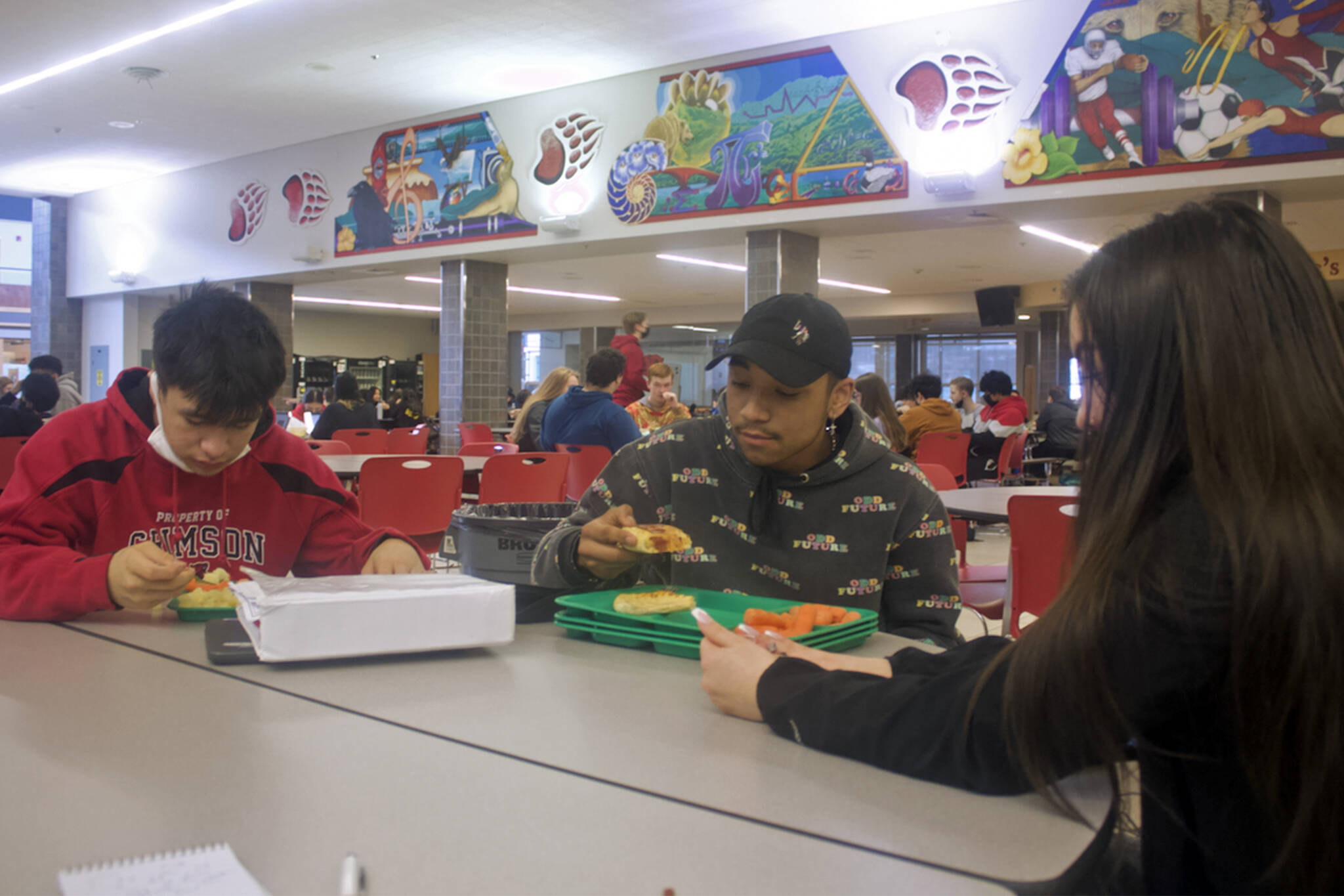 A.J. Wilson, 17, DeAndre Pittman, 16, and Elora Johnson, 16, eat lunch Thursday in the Juneau-Douglas High School: Yadaa.at Kalé cafeteria. They, like many students, agree the free meals available during the pandemic are worth continuing if funding can be found after it ends June 30, but they are likely to look off-campus for food if they are required to pay for school lunches again. (Mark Sabbatini / Juneau Empire)