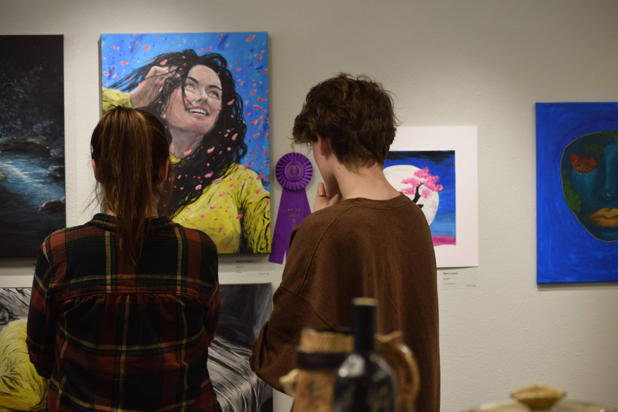 Community members look at artwork on display during the opening reception of the Kenai Art Center’s annual student show on Thursday, April 7, 2022. (Camille Botello/Peninsula Clarion)