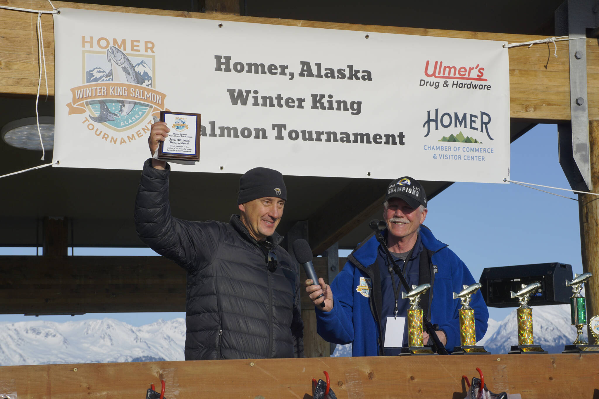 Jay Marley, left, captain of the Fly Dough, holds up the John Hillstrand Memorial Award for running the boat that had the winning fish in the 28th annual Homer Winter King Salmon Tournament. Homer Chamber of Commerce and Visitor Center executive director Brad Anderson is at right. Marley’s son, Weston Marley, won the top prize with a 27.38-pound king salmon. Jay Marley also was the top captain in 2021 when his son Andrew also won the tournament. (Photo by Michael Armstrong/Homer News)