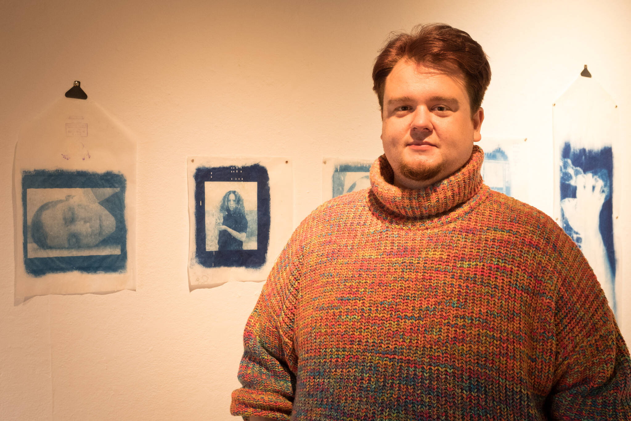 Visual artist Jesse Egner poses for a portrait in front of a series of his cyanotype prints on vintage player piano paper at Bunnell Street Arts Center in Homer, Alaska. (Photo by Sean McDermott)