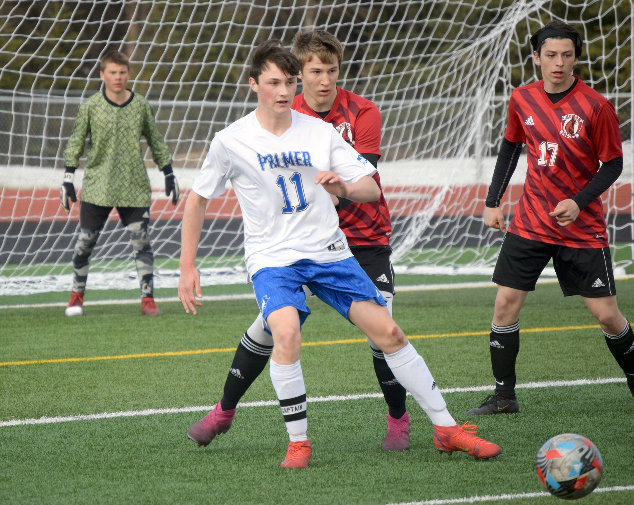 Palmer’s Xander Logan plays the ball back in front of Kenai Central’s Bridger Beck and Daniel Shelden on Friday, April 29, 2022, at Kenai Central High School in Kenai, Alaska. (Photo by Jeff Helminiak/Peninsula Clarion)