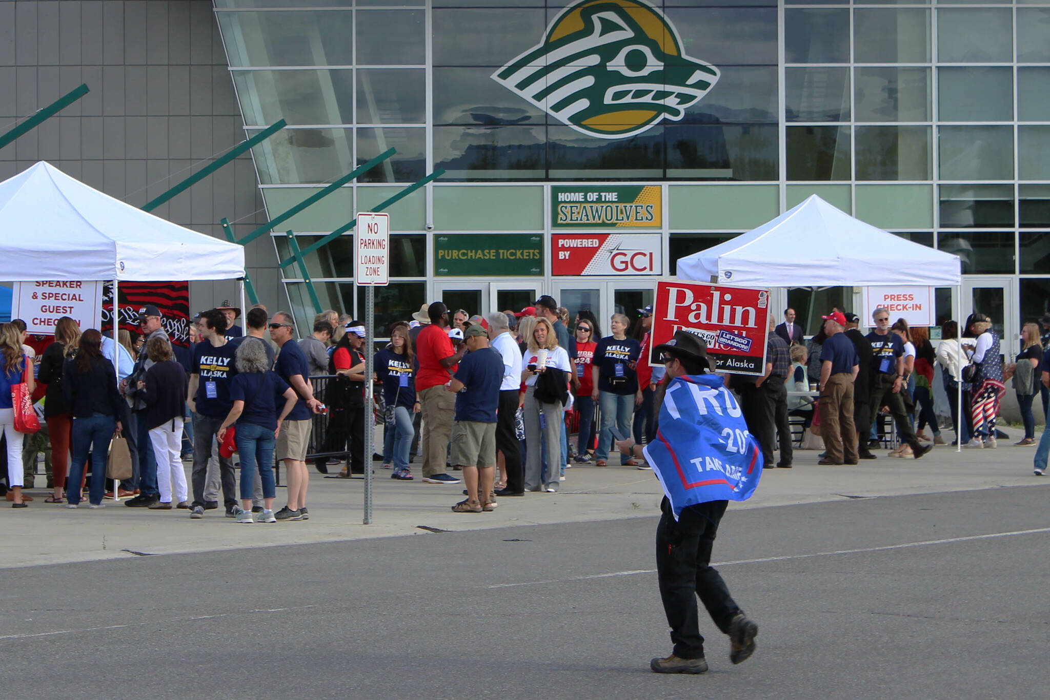A man wearing a Trump flag crosses the street in front of the Alaska Airlines Center, where a Save America rally was being held, on Saturday, July 9, 2022, in Anchorage, Alaska. Former President Donald Trump, U.S. Senate candidate Kelly Tshibaka and U.S. House candidate Sarah Palin were among the event’s speakers. (Ashlyn O’Hara/Peninsula Clarion)