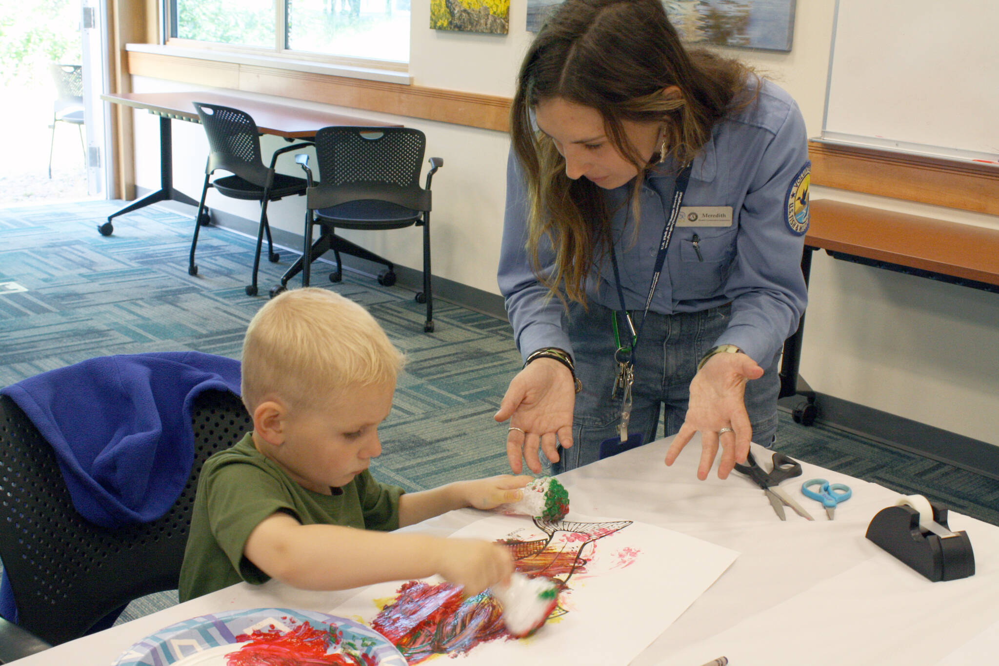 Environmental Education and Visitor Services Intern Meredith Baker helps Blake Voss, 3, paint during Fish Week at the Kenai National Wildlife Refuge in Soldotna, Alaska, on Monday, July 18, 2022. (Camille Botello/Peninsula Clarion)