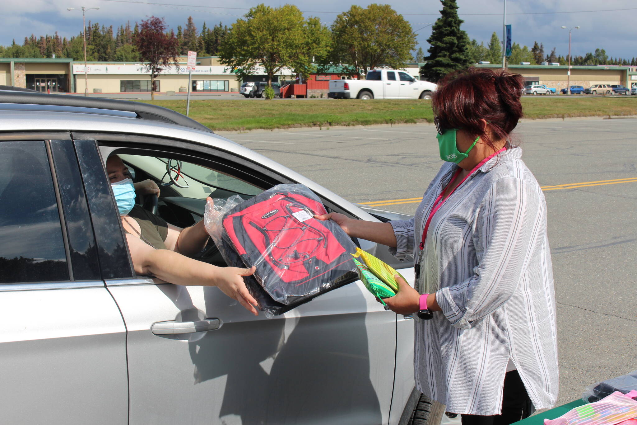 Chastity Swafford, right, gives a free backpack and school supplies to Heather Perry, left, as part of Peninsula Community Health Center’s drive-thru backpack giveaway in Kenai, Alaska on Aug. 19, 2020. (Photo by Brian Mazurek/Peninsula Clarion file)