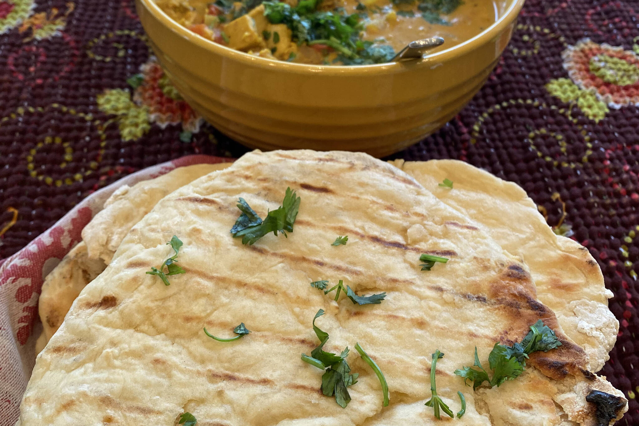 Homemade garlic naan is served with a meal of palak tofu, butter chicken, basmati rice and cucumber salad. (Photo by Tressa Dale/Peninsula Clarion)