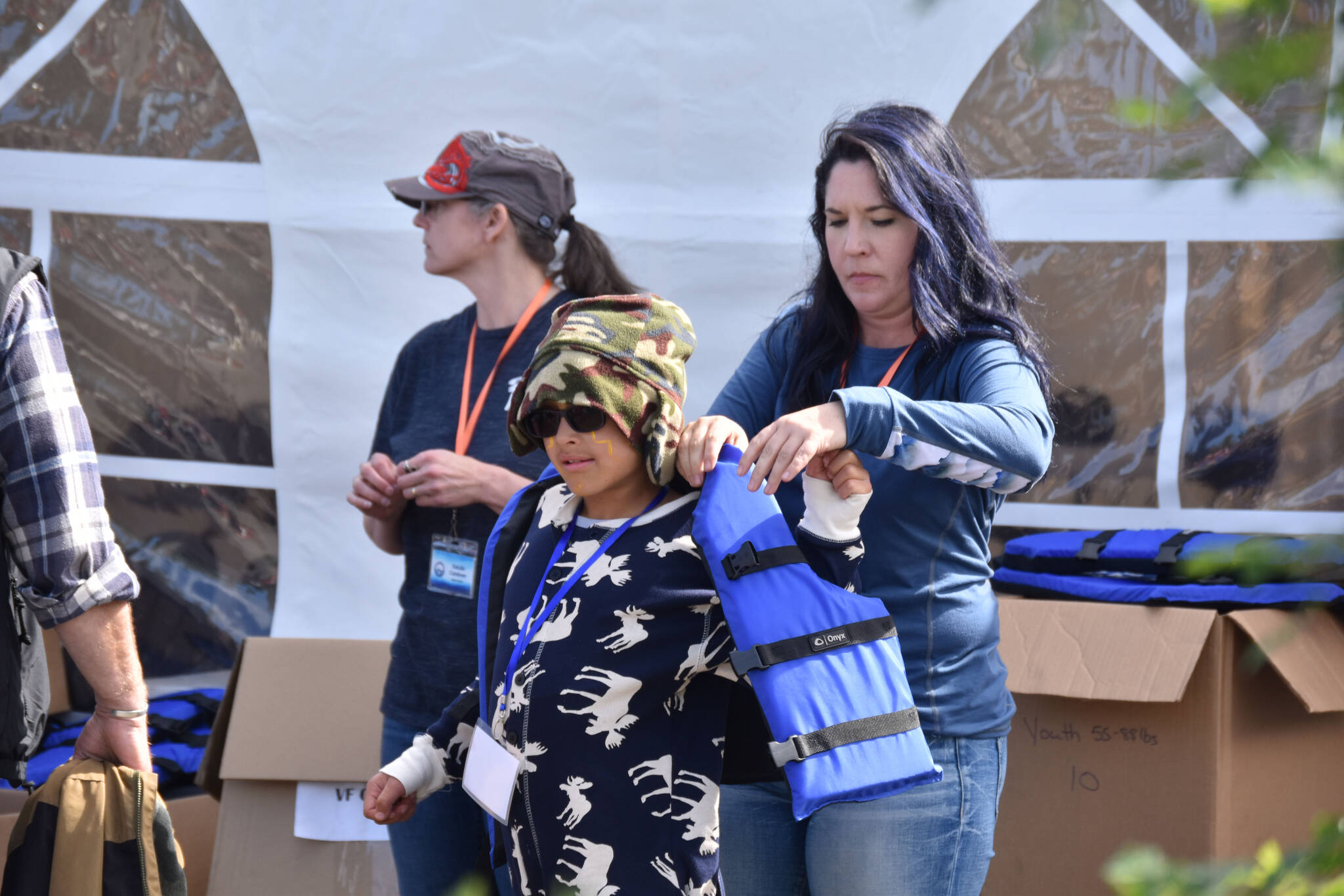 Summer Lazenby fits a child with a life jacket at the Kenai River Junior Classic in Soldotna, Alaska, on Aug. 10, 2022. (Jake Dye/Peninsula Clarion)