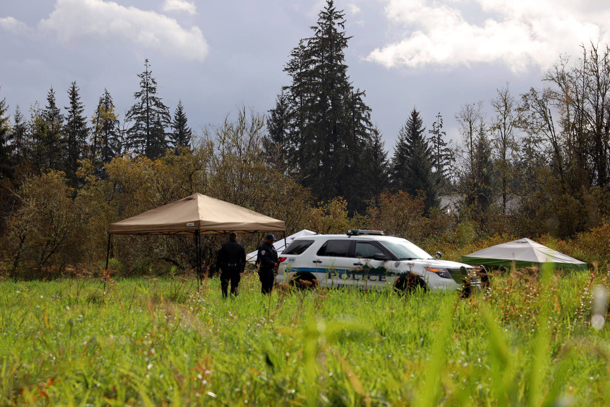 Clarise Larson / Juneau Empire
On Thursday morning at what police described as an active crime scene, JPD Officer Austin Thomas and Officer Taylor Davis walk the fielded area which was blocked off by crime scene tape. Multiple tents and a police vehicle sat in the field where the tape surrounded, another police vehicle sat in a dirt parking area.