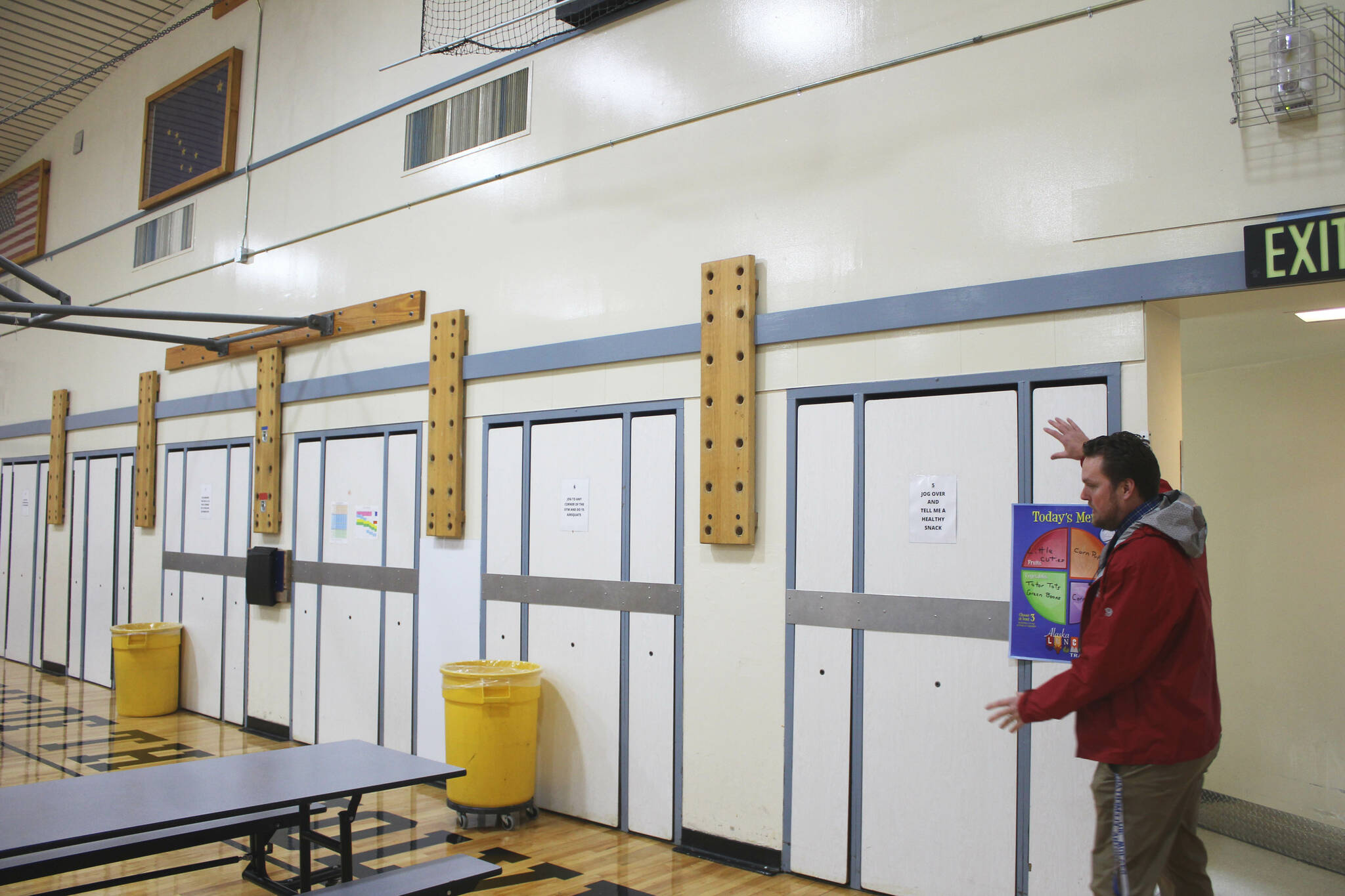 Soldotna Elementary School Principal Dr. Austin Stevenson gestures to lunch tables that are nailed into the gym wall on Friday, Sept. 30, 2022, in Soldotna, Alaska. (Ashlyn O’Hara/Peninsula Clarion)