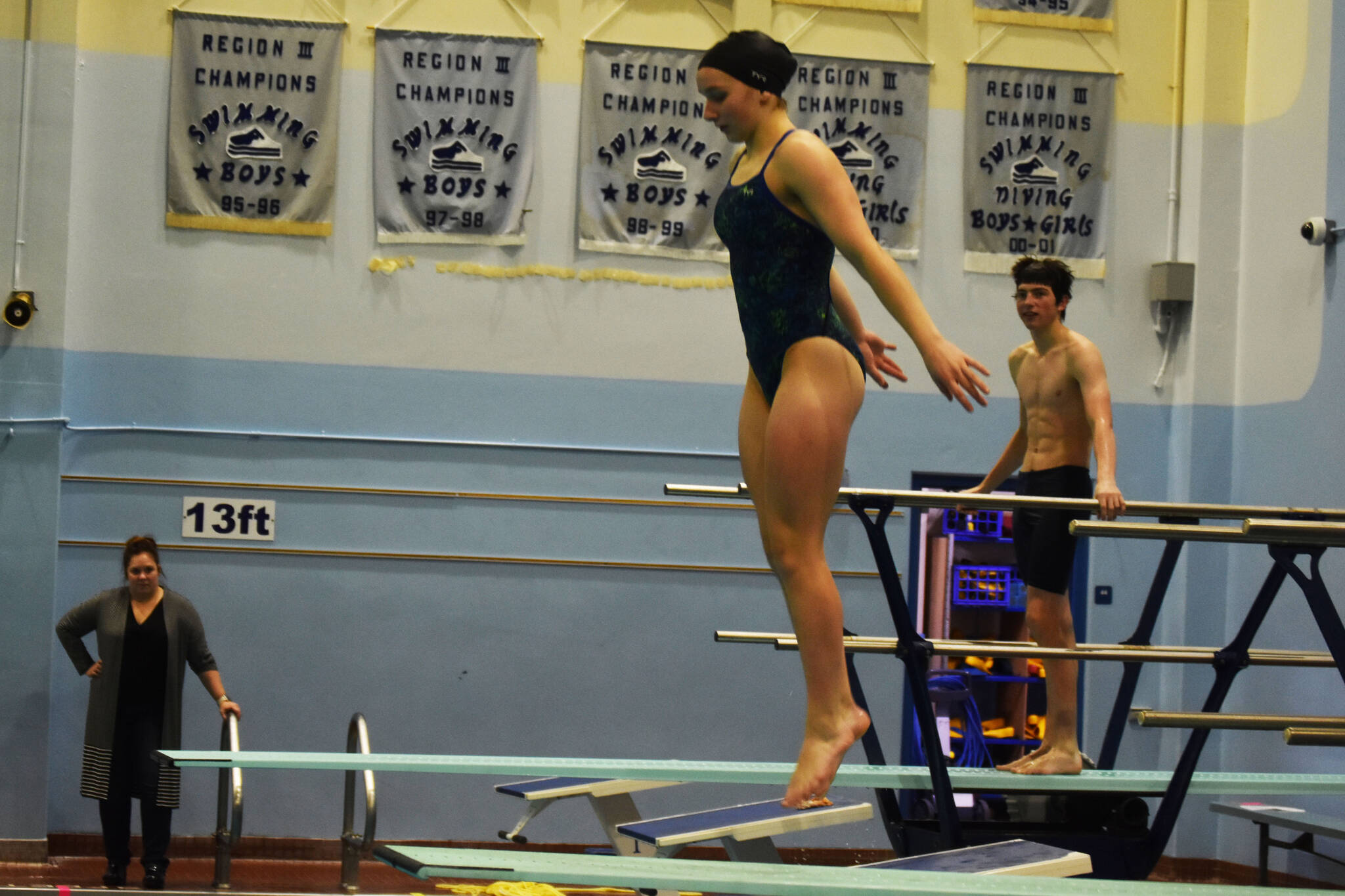 Abriella Werner leaps as she approaches the end of the diving board, Shonia Werner and Derrick Jones watch during a dive practice on Tuesday, Oct. 11, 2022, at Soldotna High School in Soldotna, Alaska. (Jake Dye/Peninsula Clarion)