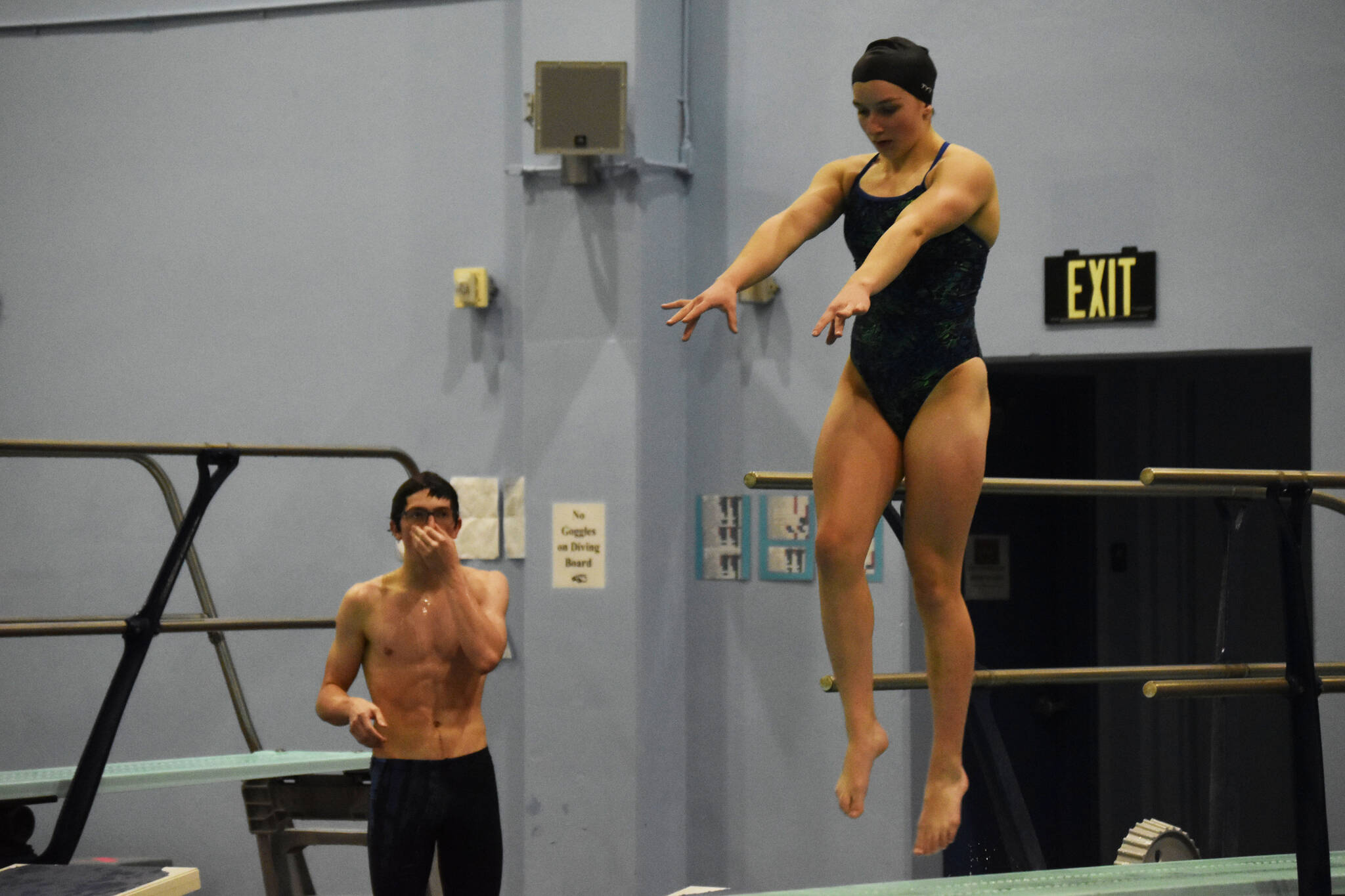Abriella Werner leaps as she approaches the end of the diving board, Derrick Jones watches during a dive practice on Tuesday, Oct. 11, 2022, at Soldotna High School in Soldotna, Alaska. (Jake Dye/Peninsula Clarion)