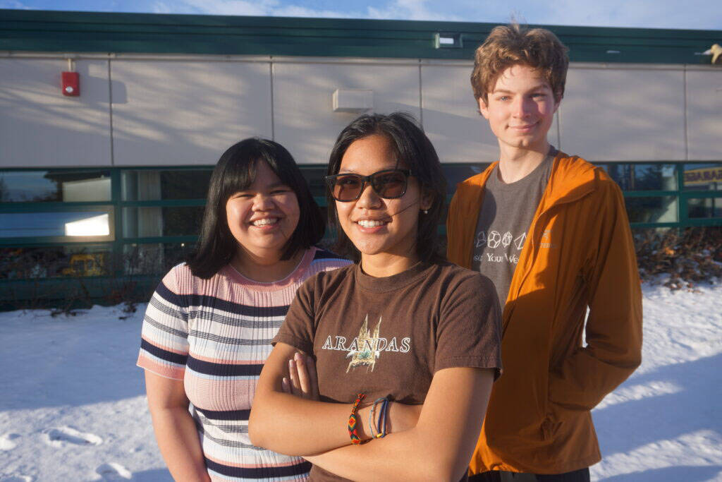 Steller Secondary School seniors gather in the sunshine outside their school on Oct. 27. From left are Pauline Mallari, Samantha Antonio and Zane Barber, all bound for college. They all enjoy the Alaska outdoors lifestyle, but they all expressed lack of confidence in Alaska as a place for young people to build careers. Demographic data shows that young adults are leaving Alaska, contributing to nine straight years of net outmigration. (Photo by Yereth Rosen/Alaska Beacon)