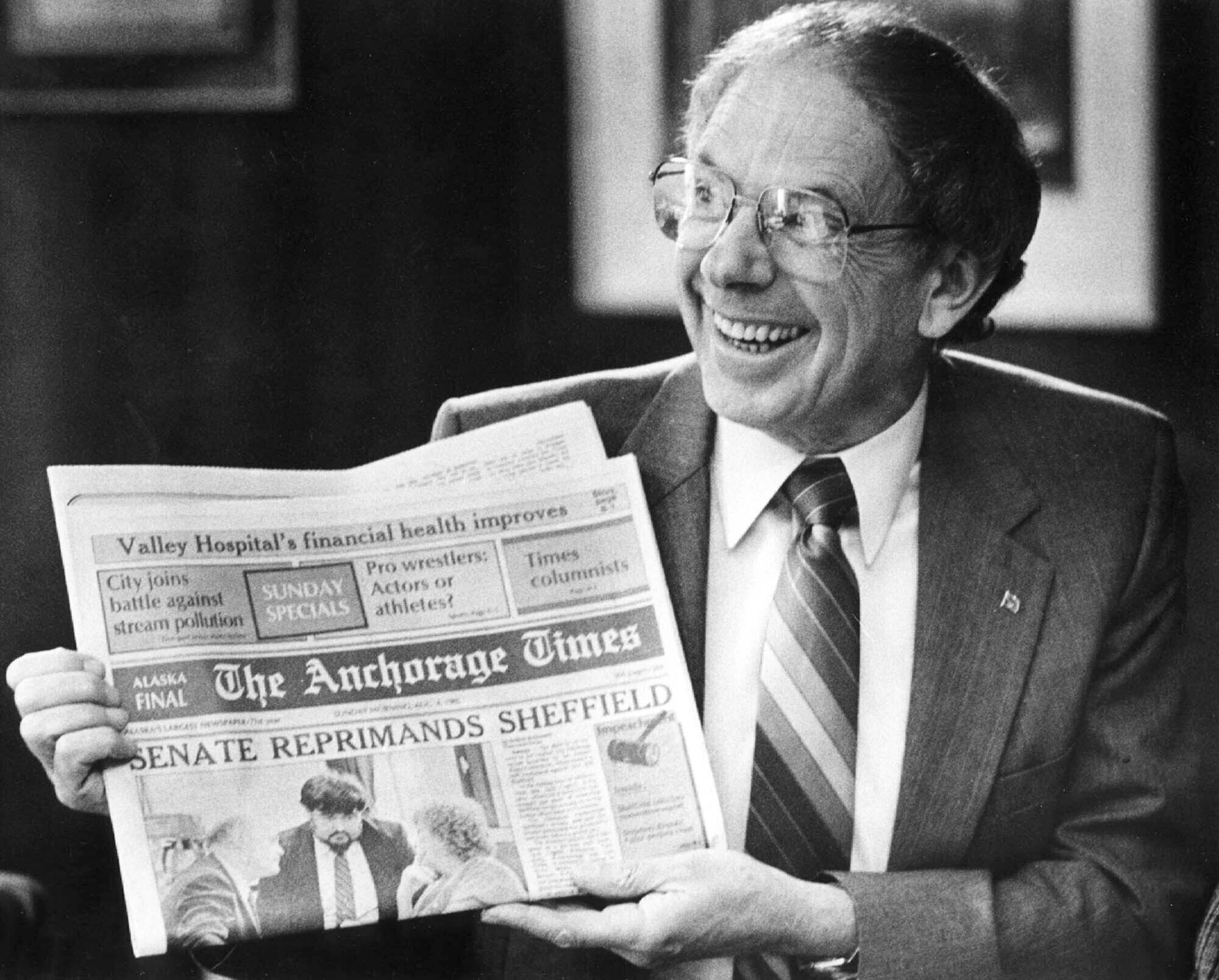 Former Alaska Gov. Bill Sheffield smiles as he holds a The Anchorage Times newspaper in his Capitol office in Juneau, Alaska, on Aug. 5, 1985, after he survived an impeachment effort during July and August 1985. A statement provided by friends says he died Friday, Nov. 4, 2022, at his home in Anchorage. He was 94. Sheffield was governor from 1982 to 1986. (Brian Wallace/The Juneau Empire via AP, File)