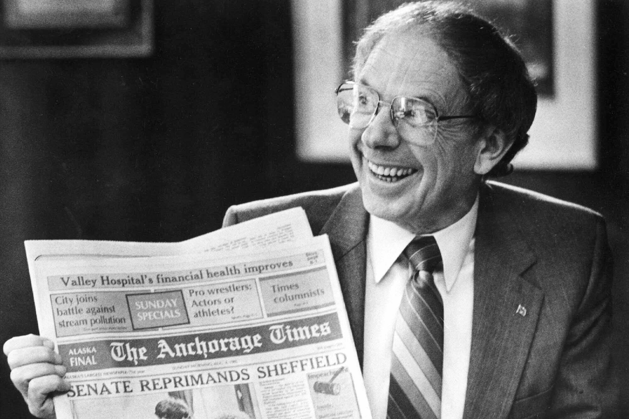 Former Alaska Gov. Bill Sheffield smiles as he holds a The Anchorage Times newspaper in his Capitol office in Juneau, Alaska, on Aug. 5, 1985, after he survived an impeachment effort during July and August 1985. A statement provided by friends says he died Friday, Nov. 4, 2022, at his home in Anchorage. He was 94. Sheffield was governor from 1982 to 1986. (Brian Wallace/The Juneau Empire via AP, File)